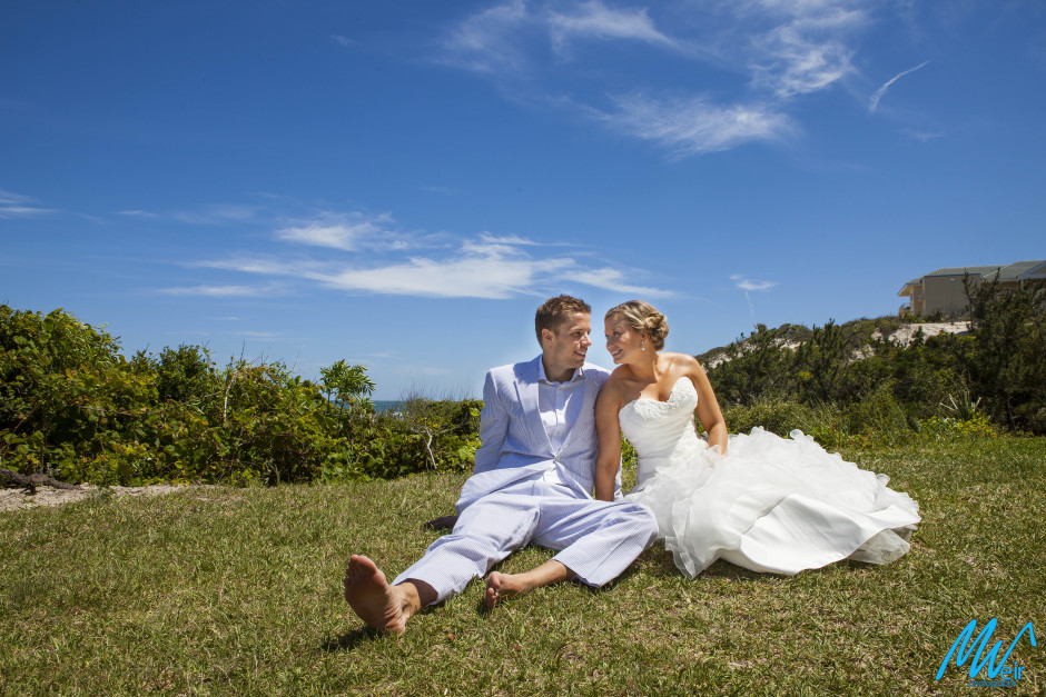bride and groom sitting on top of a hill looking into each others eyes with a blue sky in the background