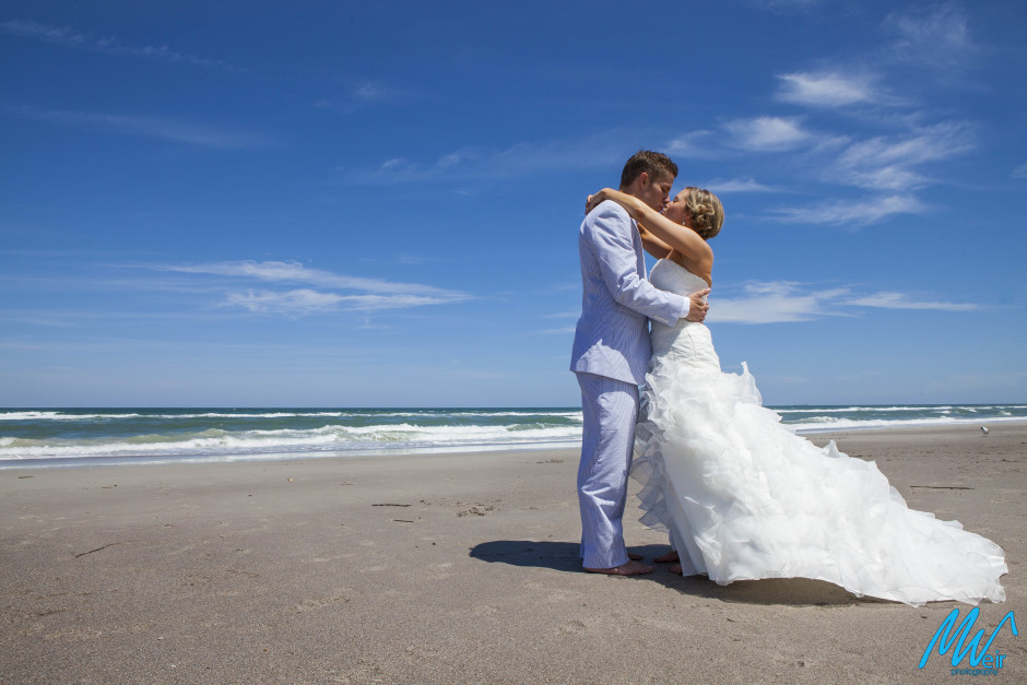 bride and groom kissing on the beach with brides dress blowing in the wind