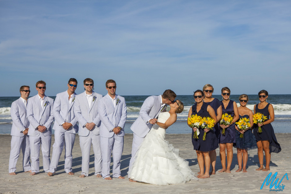 couple kissing in front of bridal party on the beach in front of the ocean