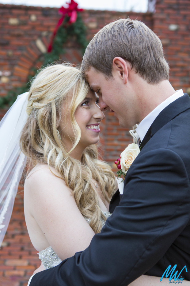bride and groom cuddle in front of brick wall