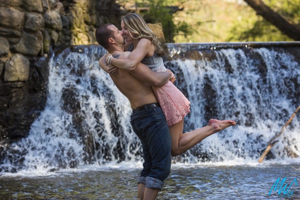 groom holding bride up in the water in front of water fall