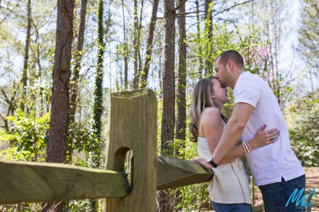 groom kissing brides forehead by an old fence
