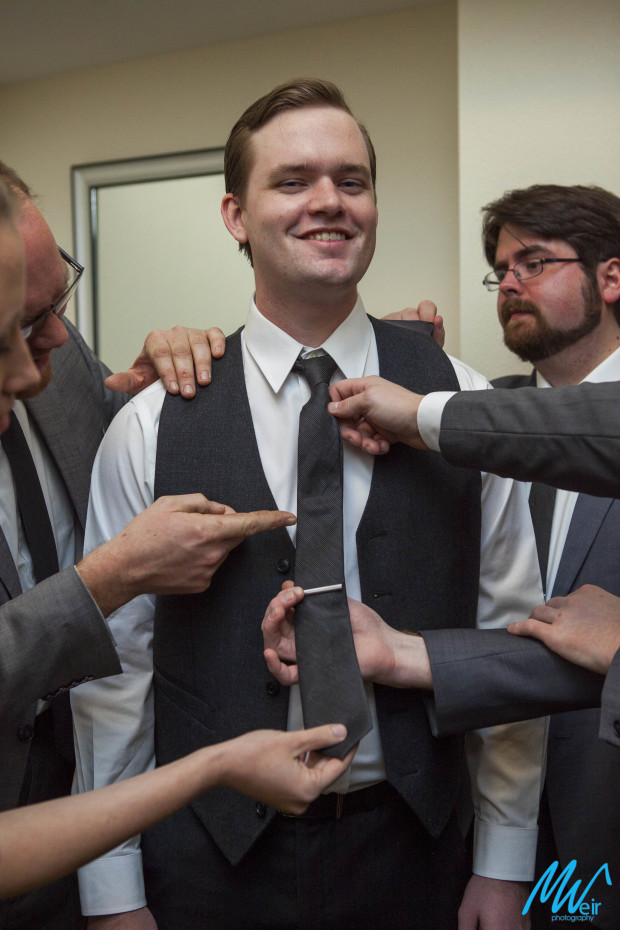 groomsman receiving help with his tie from all groomsmen