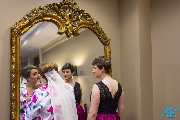 bride puts on lipgloss in the mirror with her sister next to her
