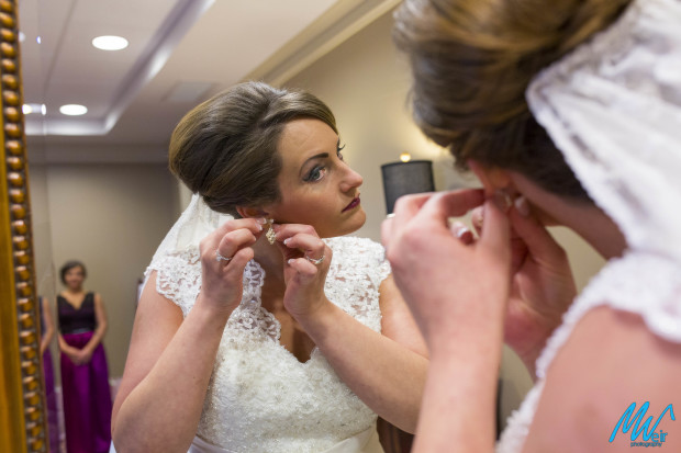 brides puts on her earrings in the mirror