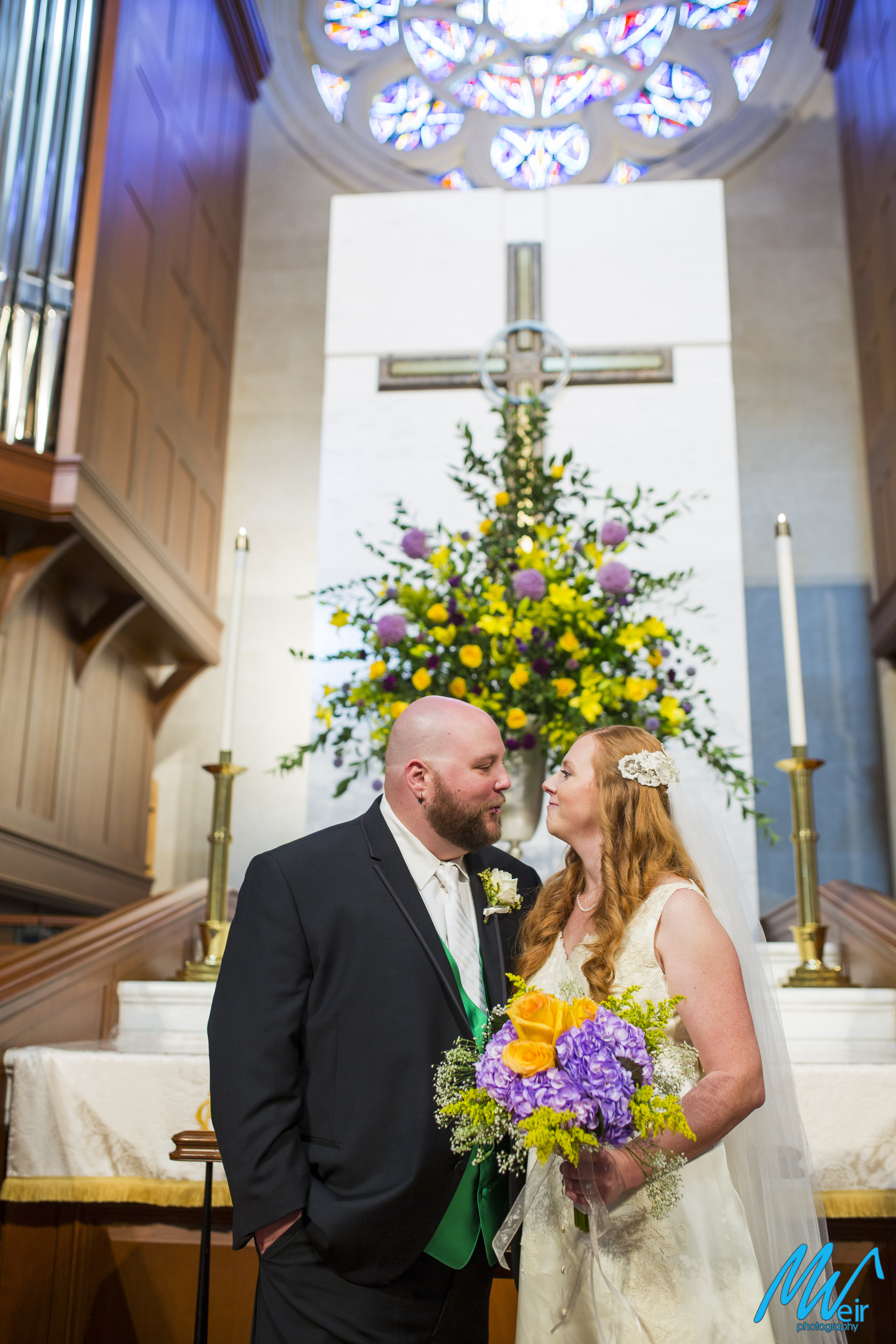 bride and groom stand in front of floral arrangement in the sanctuary