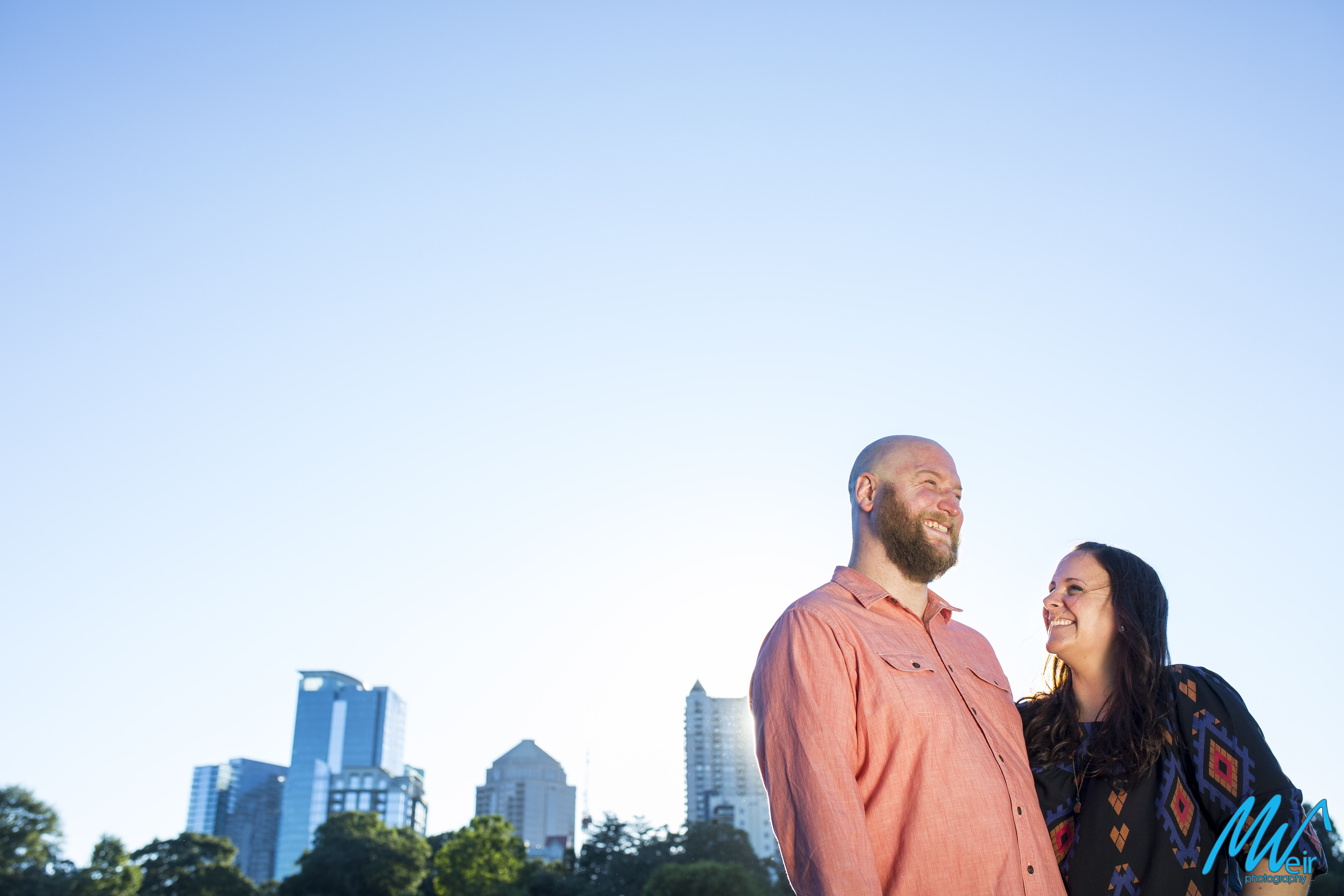 bride and groom stand in setting sun in front of skyline