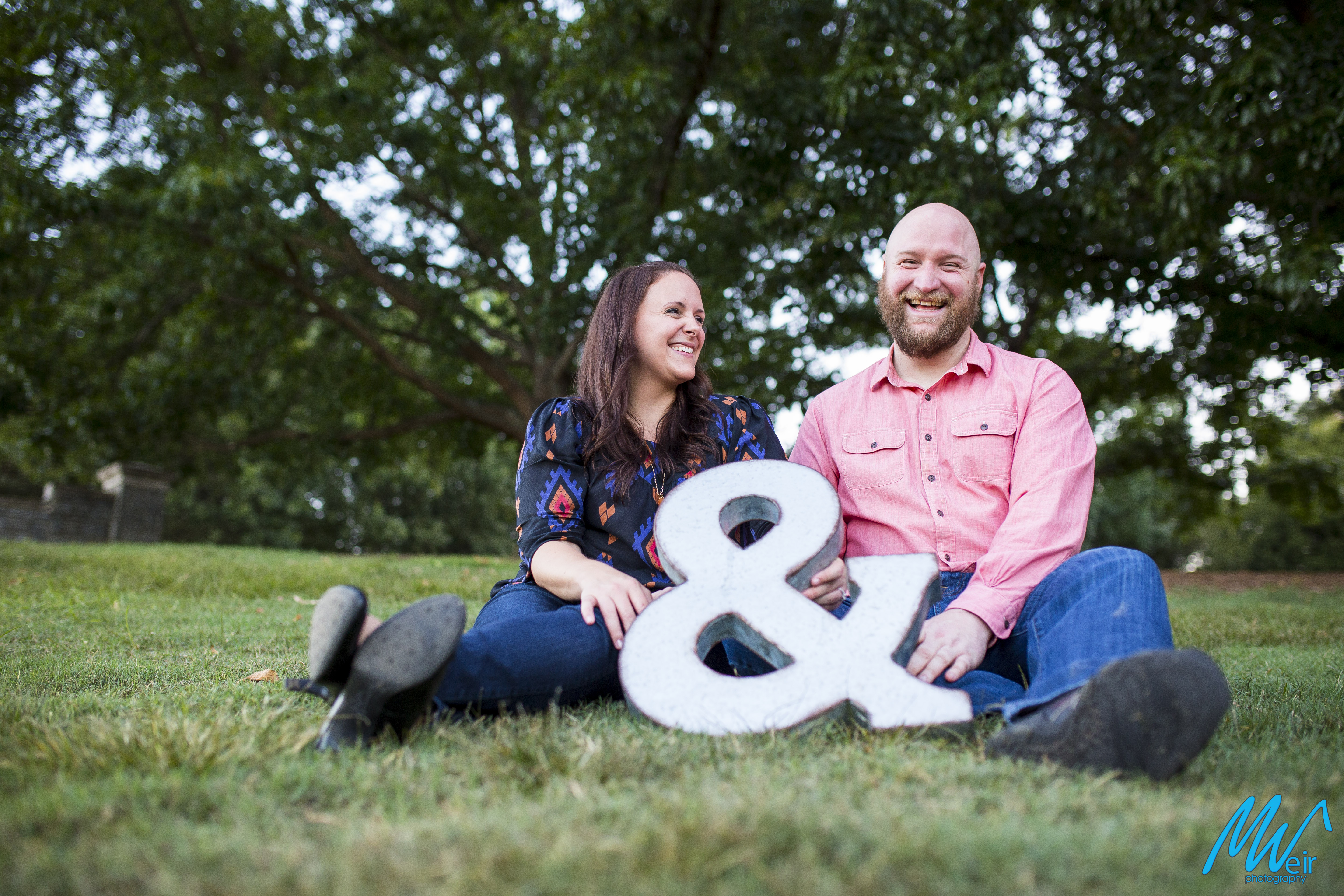 bride and groom laugh while sitting in the grass at piedmont park