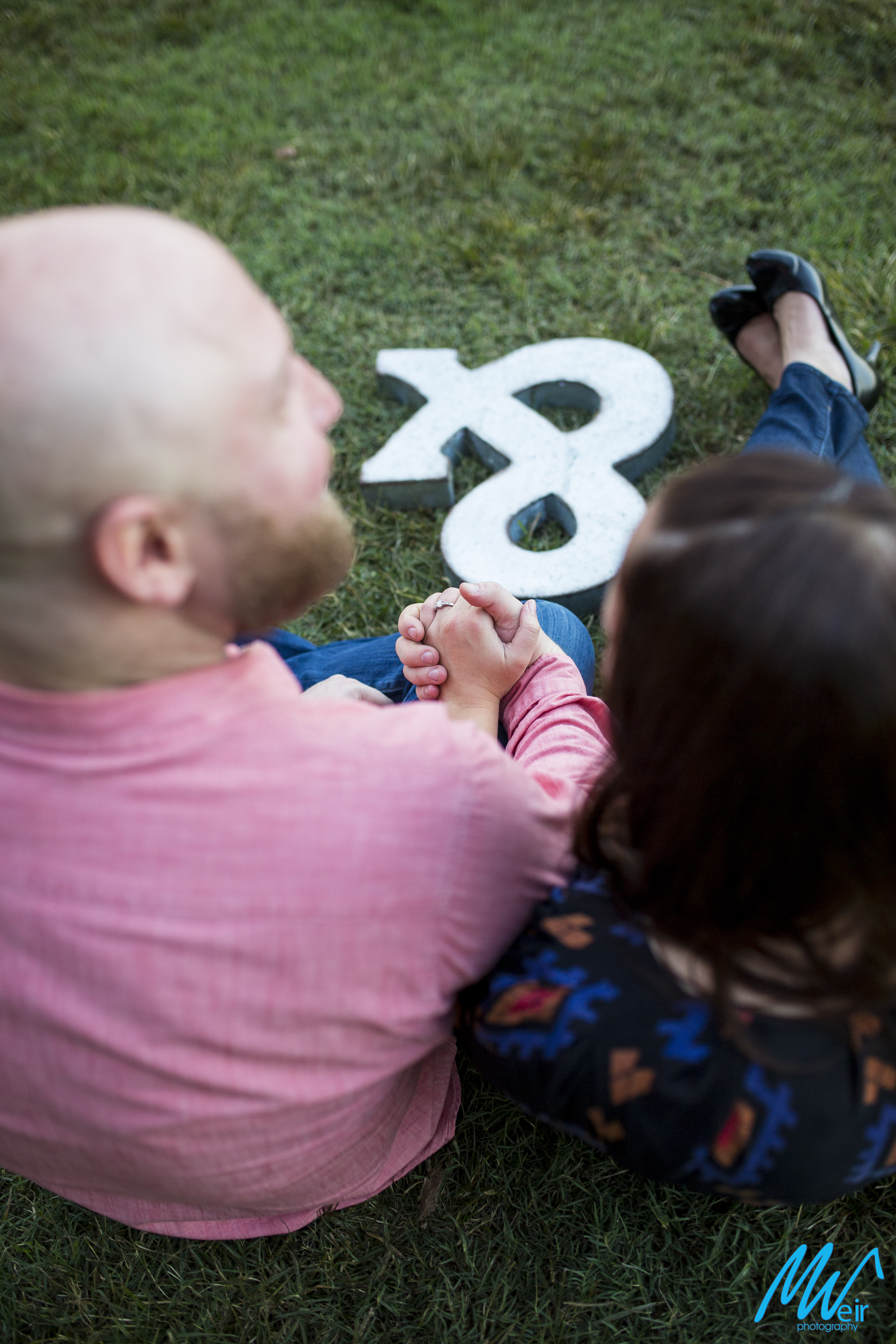 bride and groom hold hands sitting in the grass