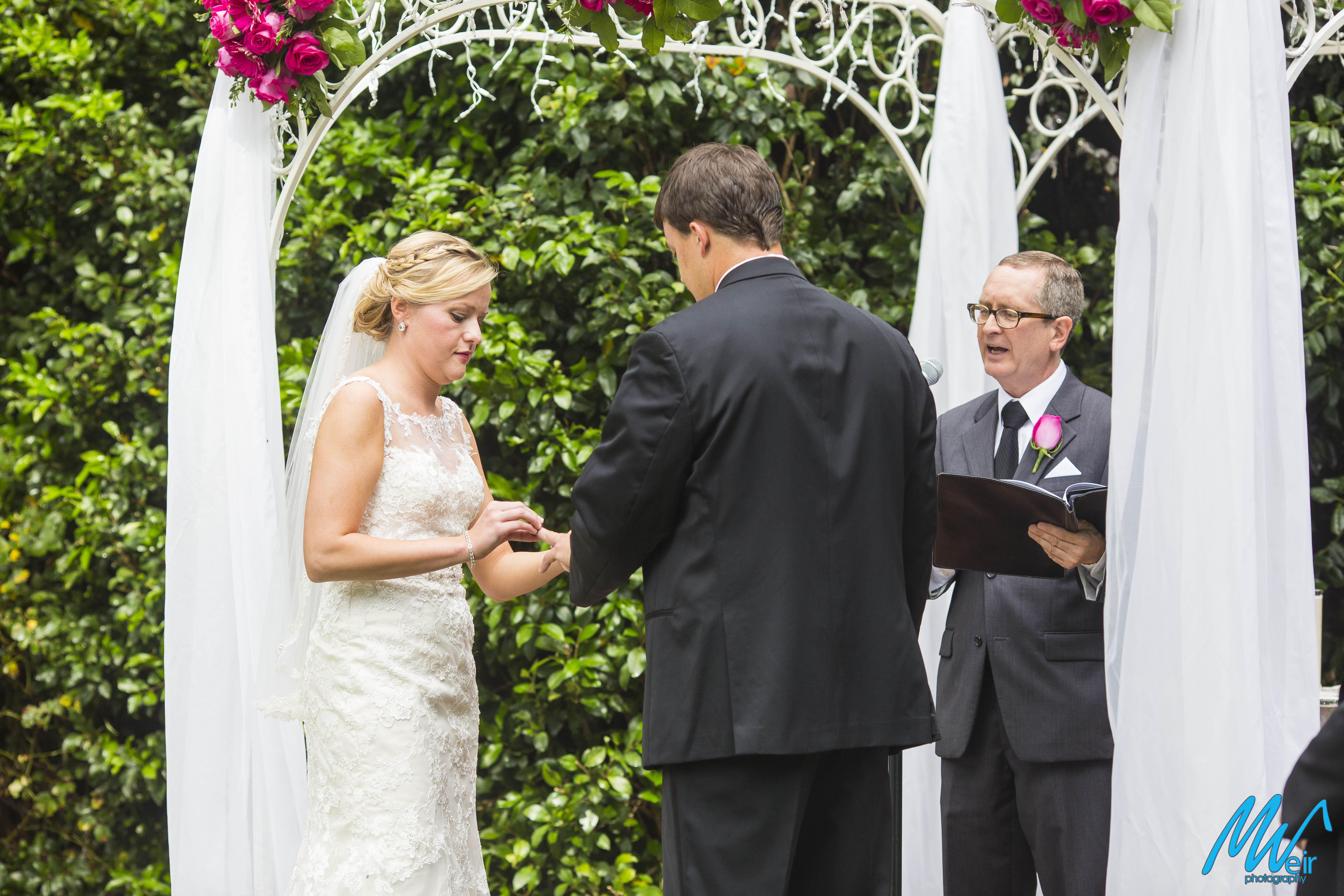 bride putting ring on grooms finger during wedding ceremony