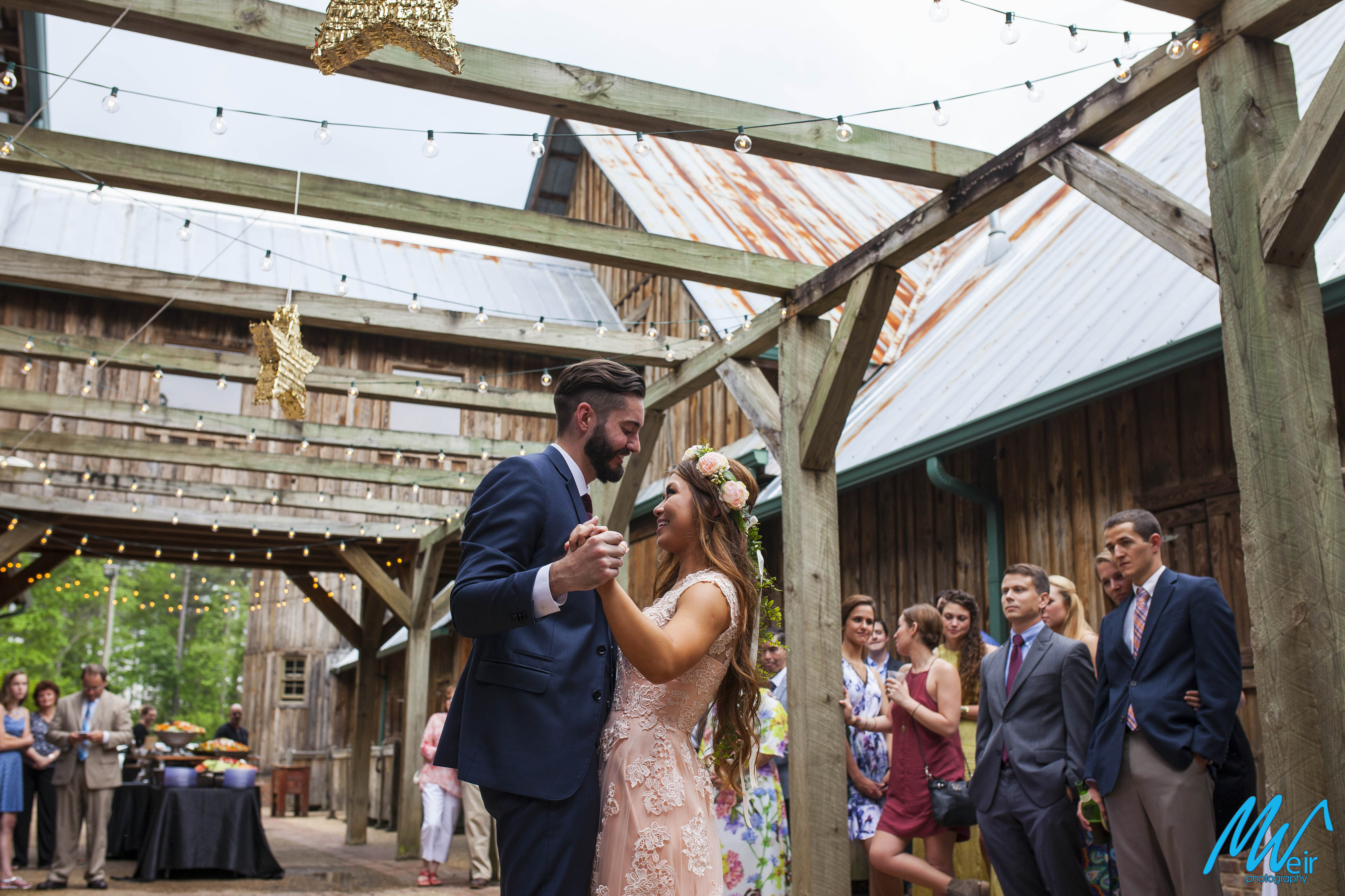 bride and groom share a first dance under wood arbor outside under star pinatas