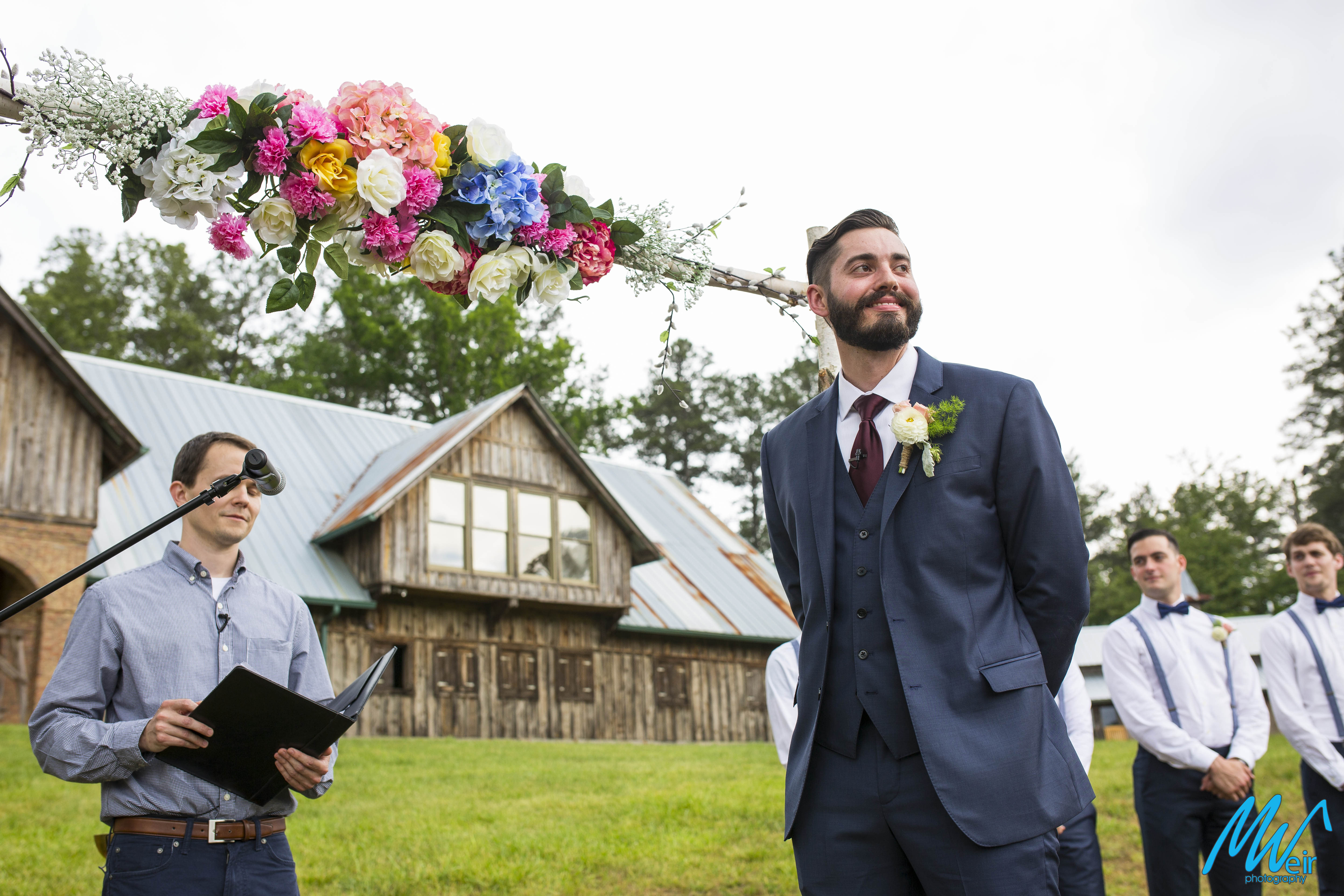 groom waits for his bride to walk to down the aisle during a boho ceremony in a field