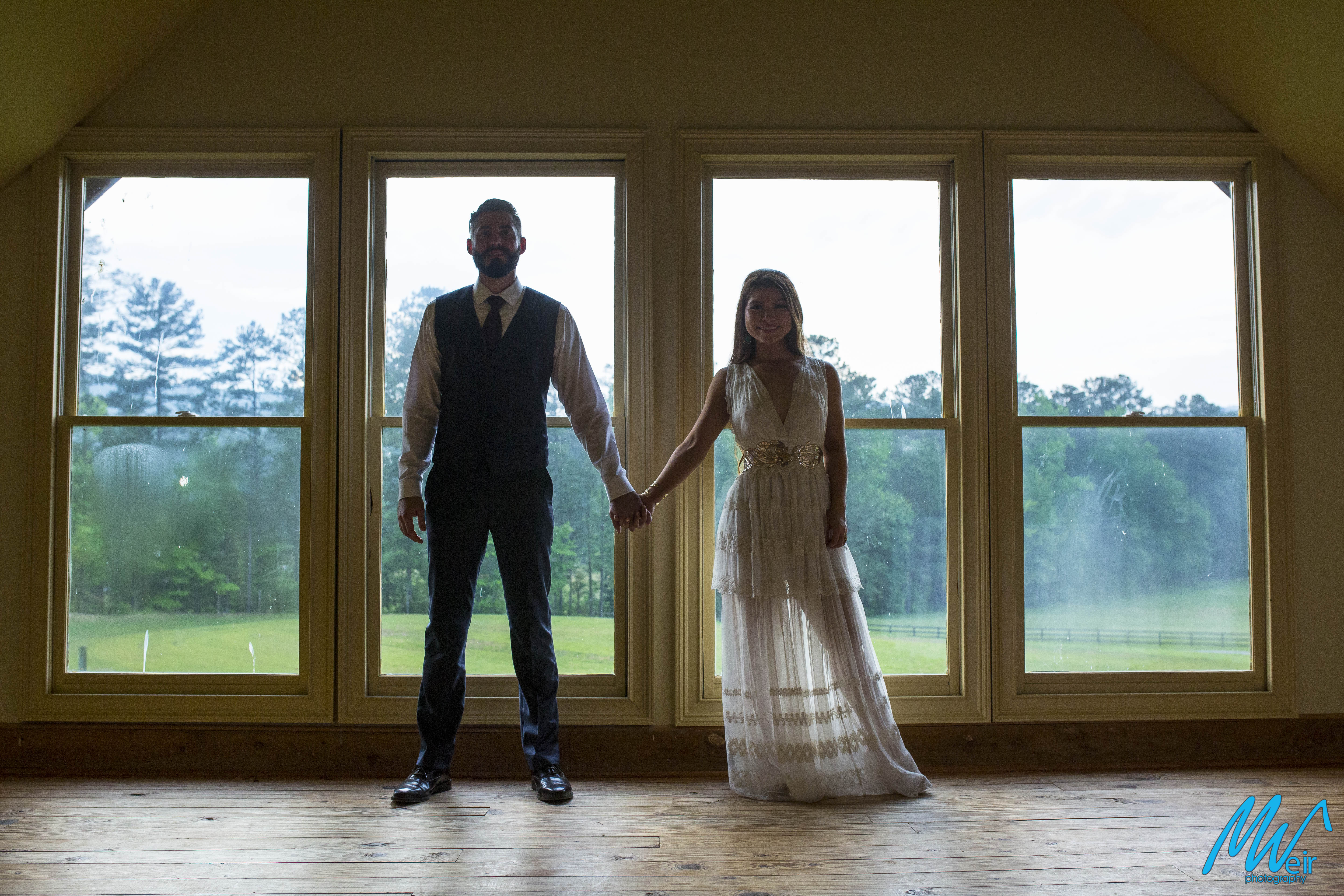 bride and groom stand in front of floor to ceiling windows