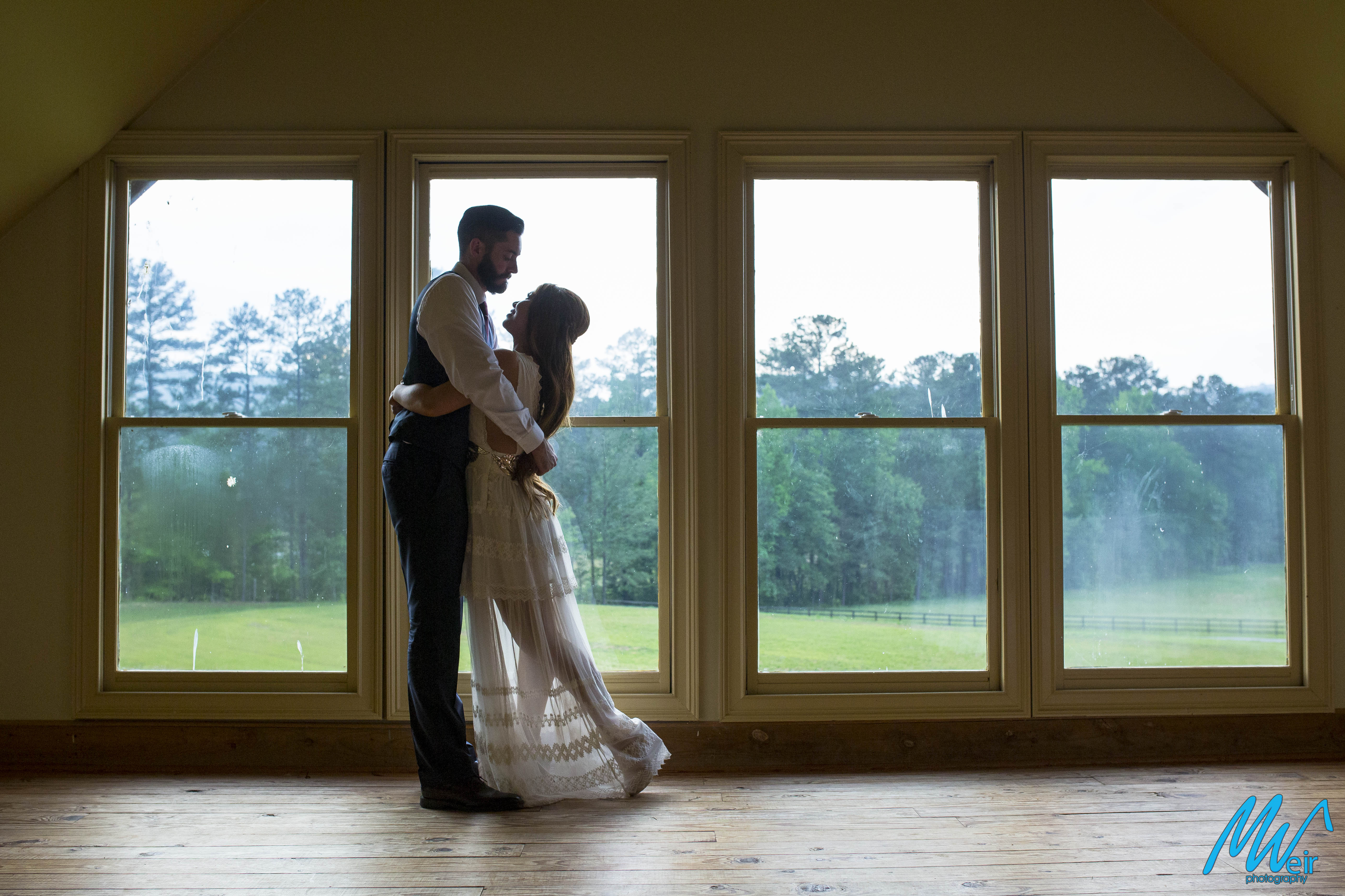 bride and groom kiss in front of floor to ceiling windows