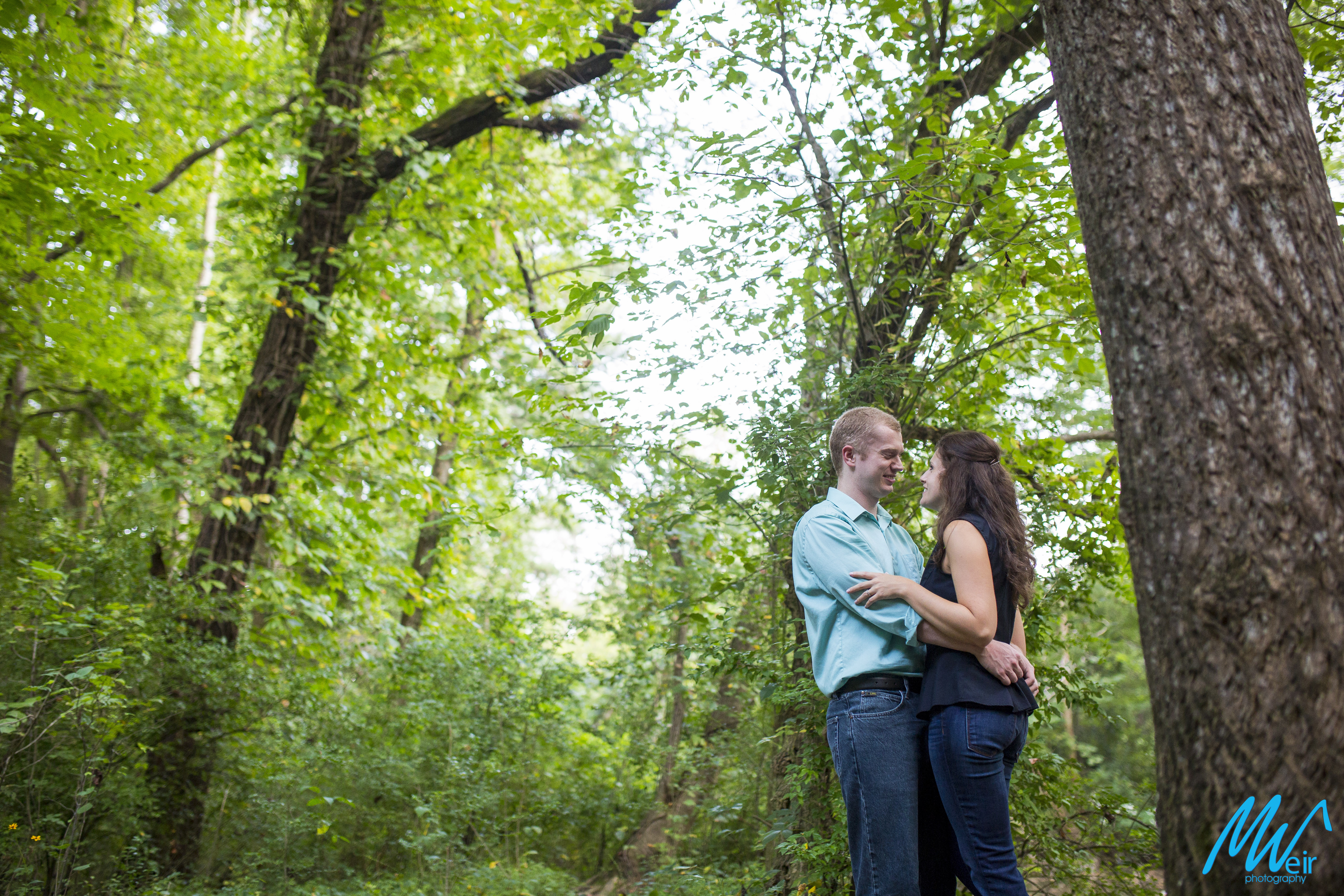 wide angle shot of bride and groom holding each other in a forest