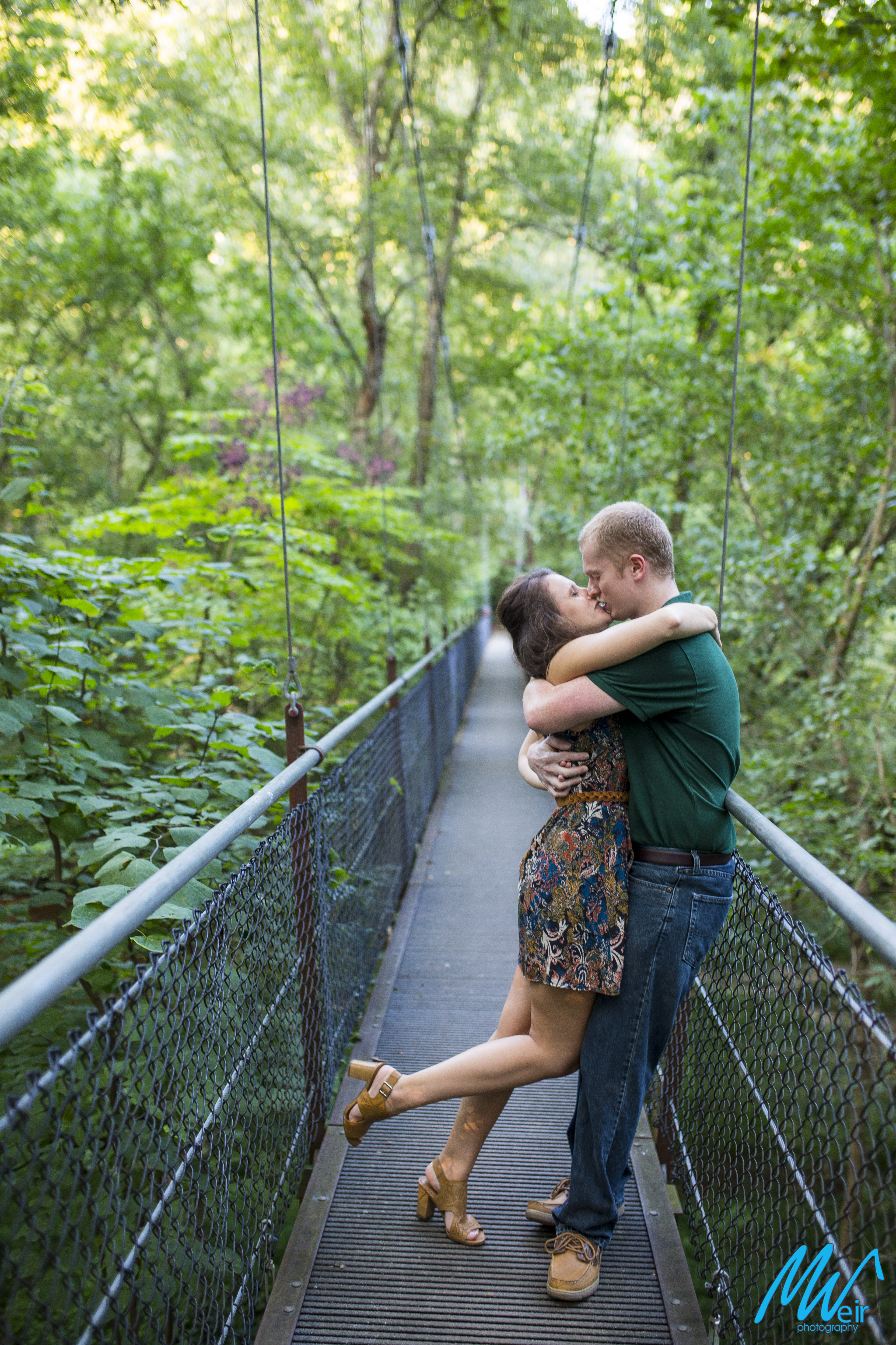 bride kisses groom on a suspension bridge in a forest