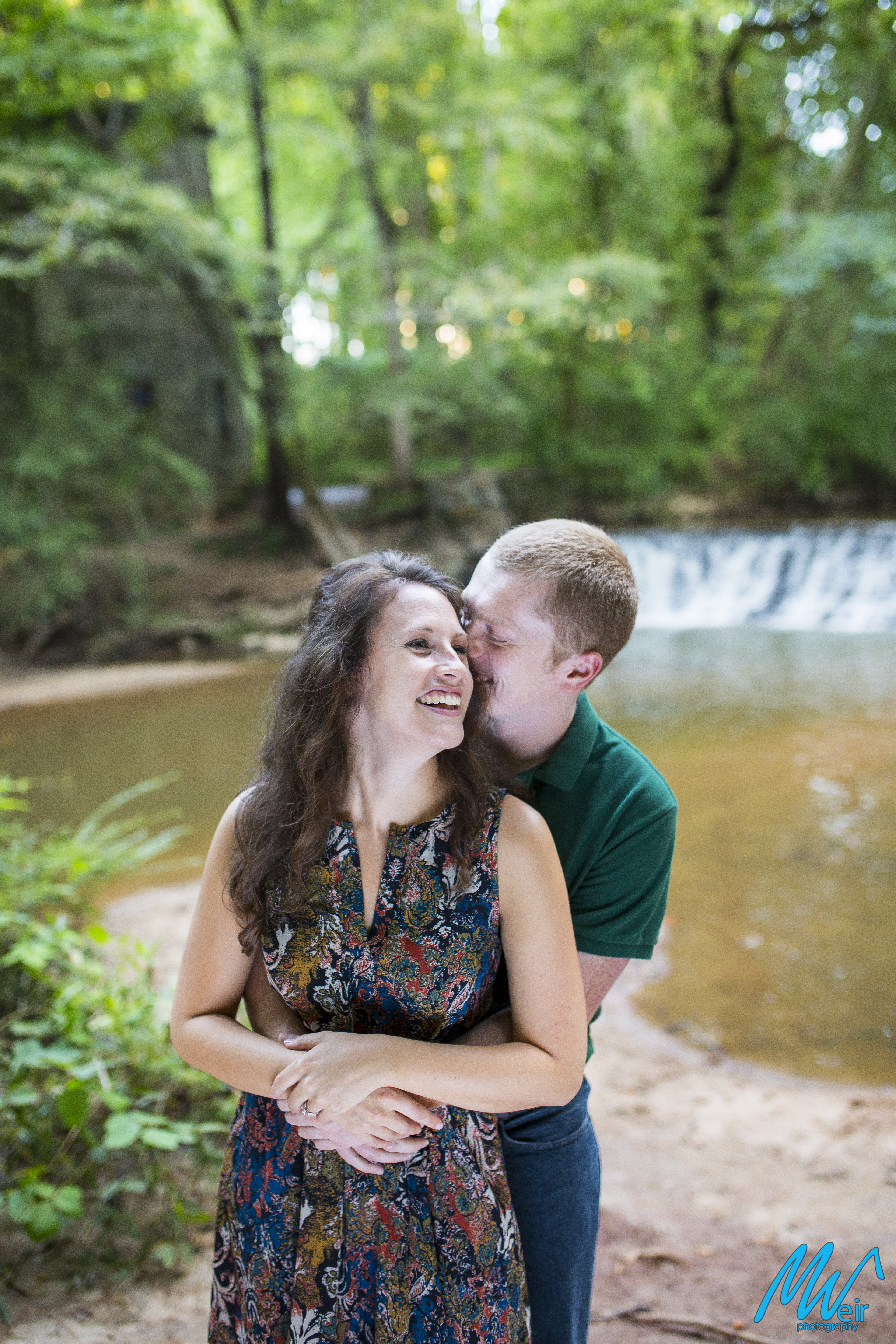 groom whispers sweet nothings in his brides ear in front of a waterfall