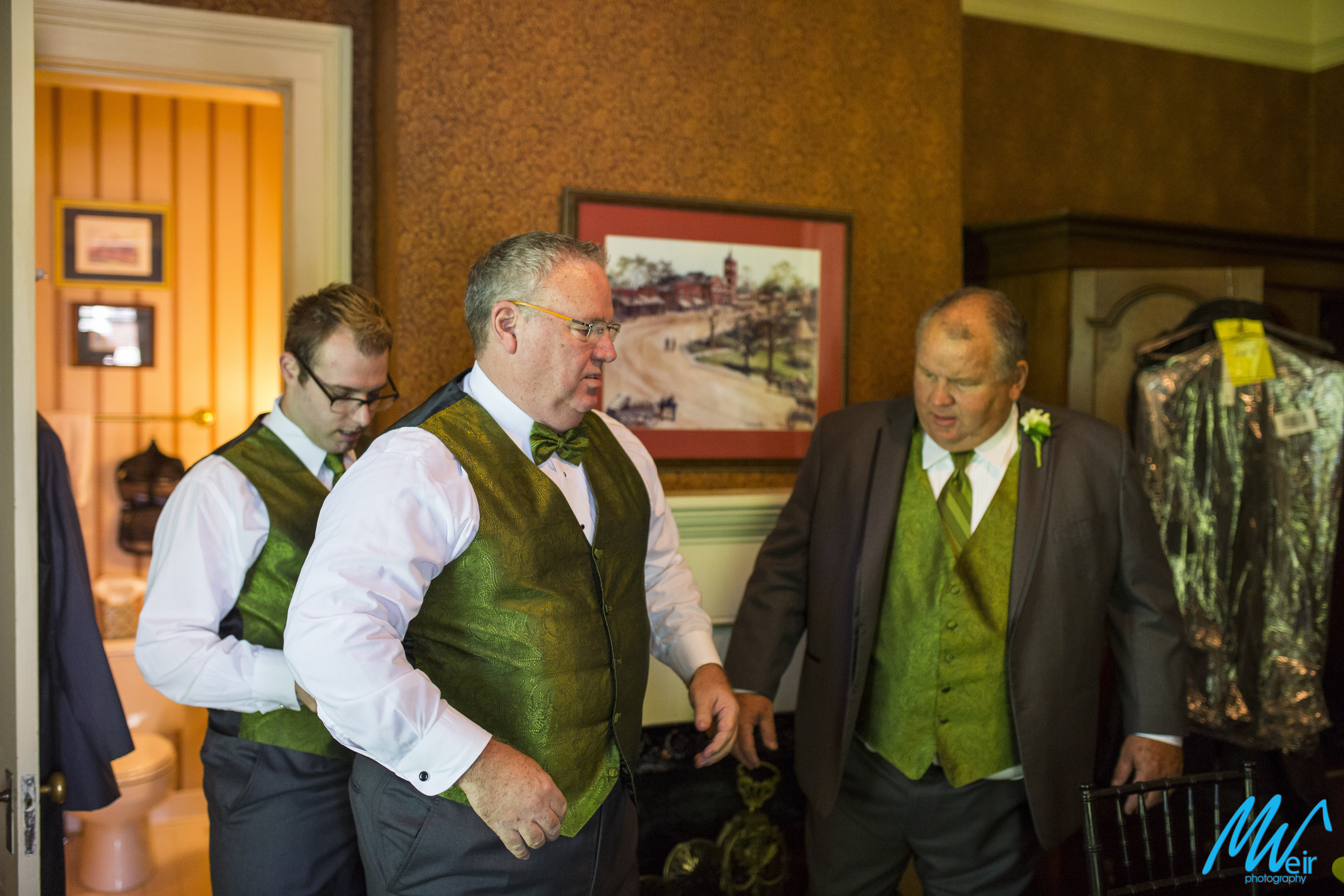 groom and groomsmen putting on their green vests and suits for wedding 