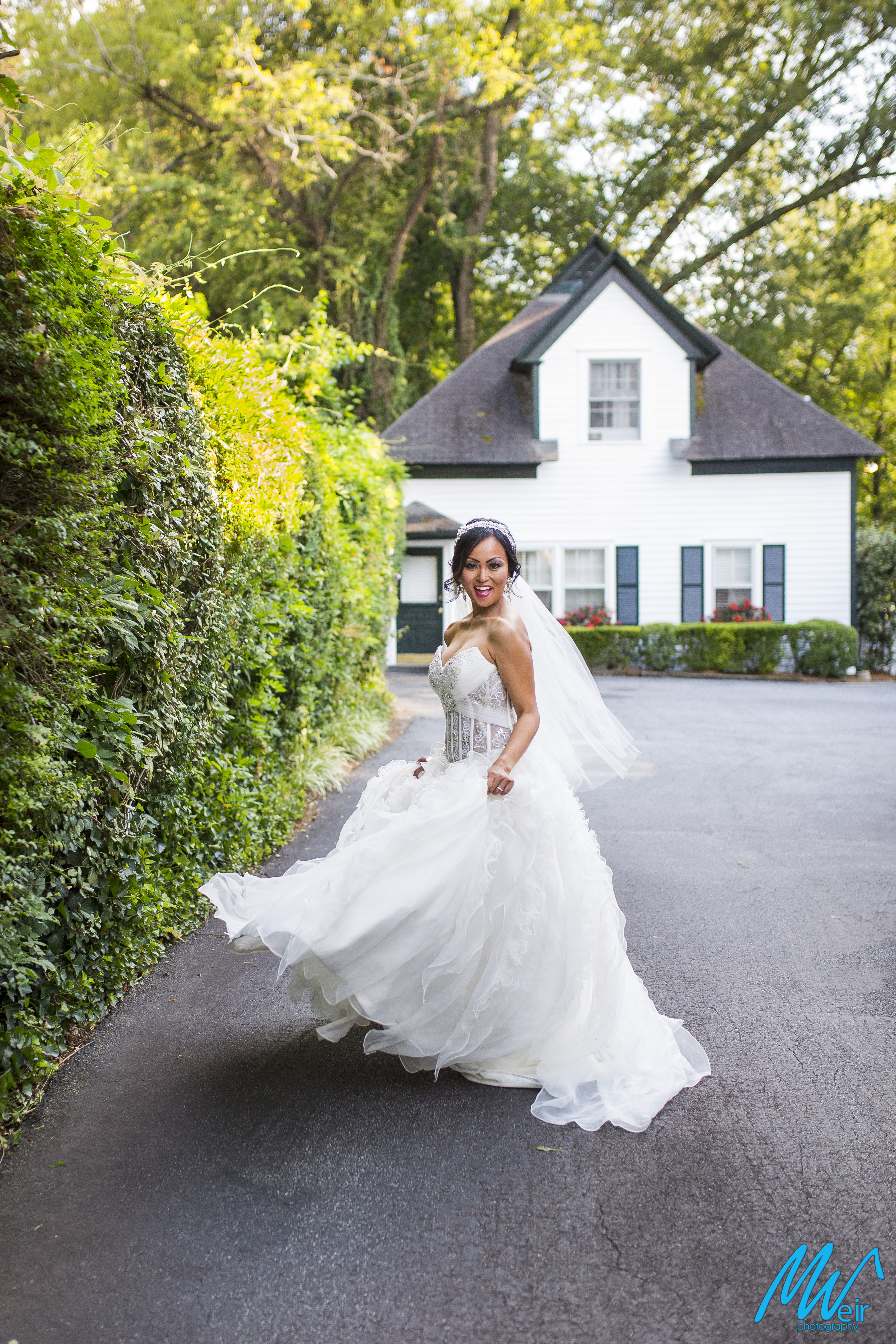 bride twirling her dress in front of cute cottage next to hedge