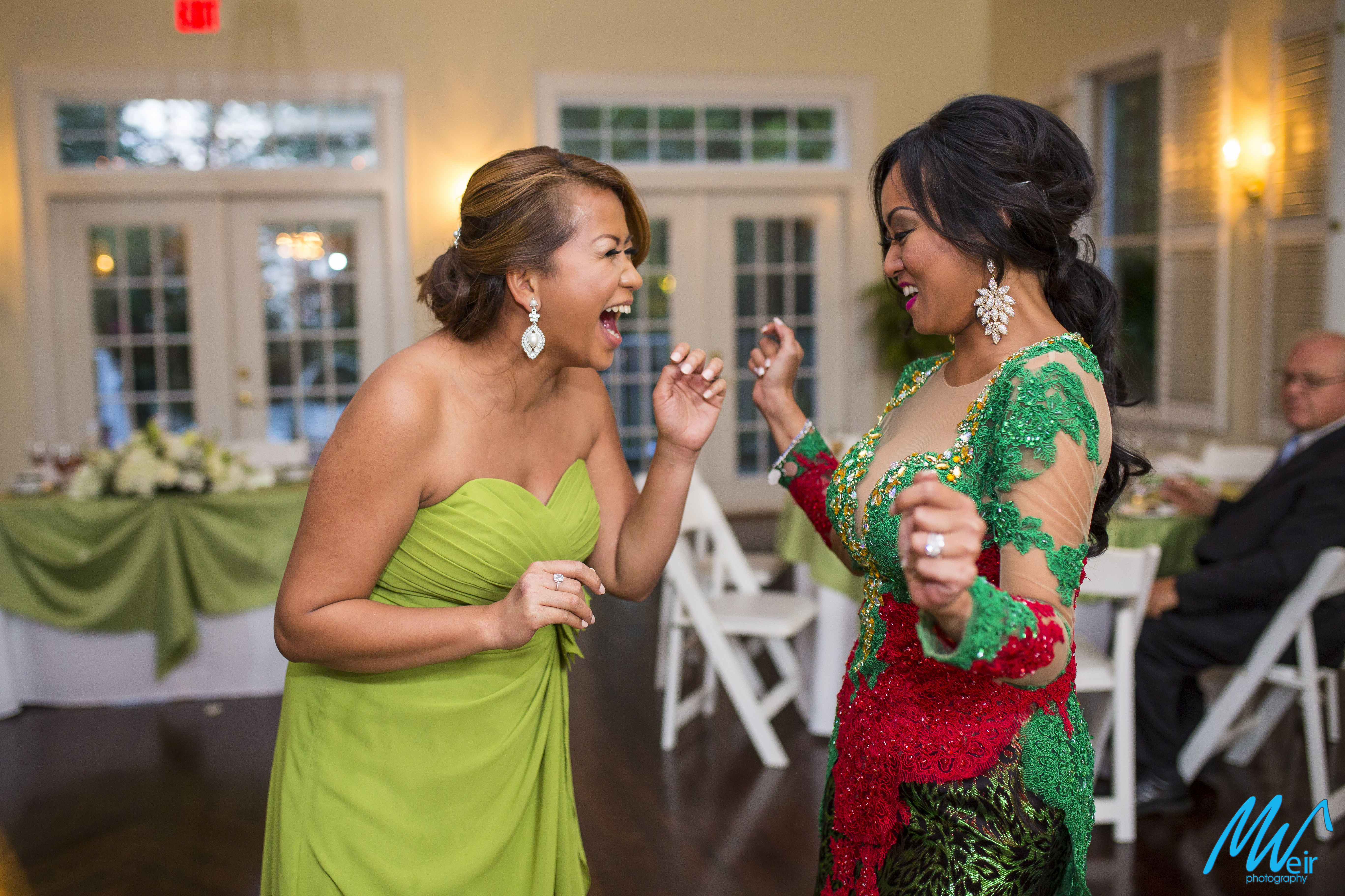 bride and maid of honor laugh and dance together at wedding reception
