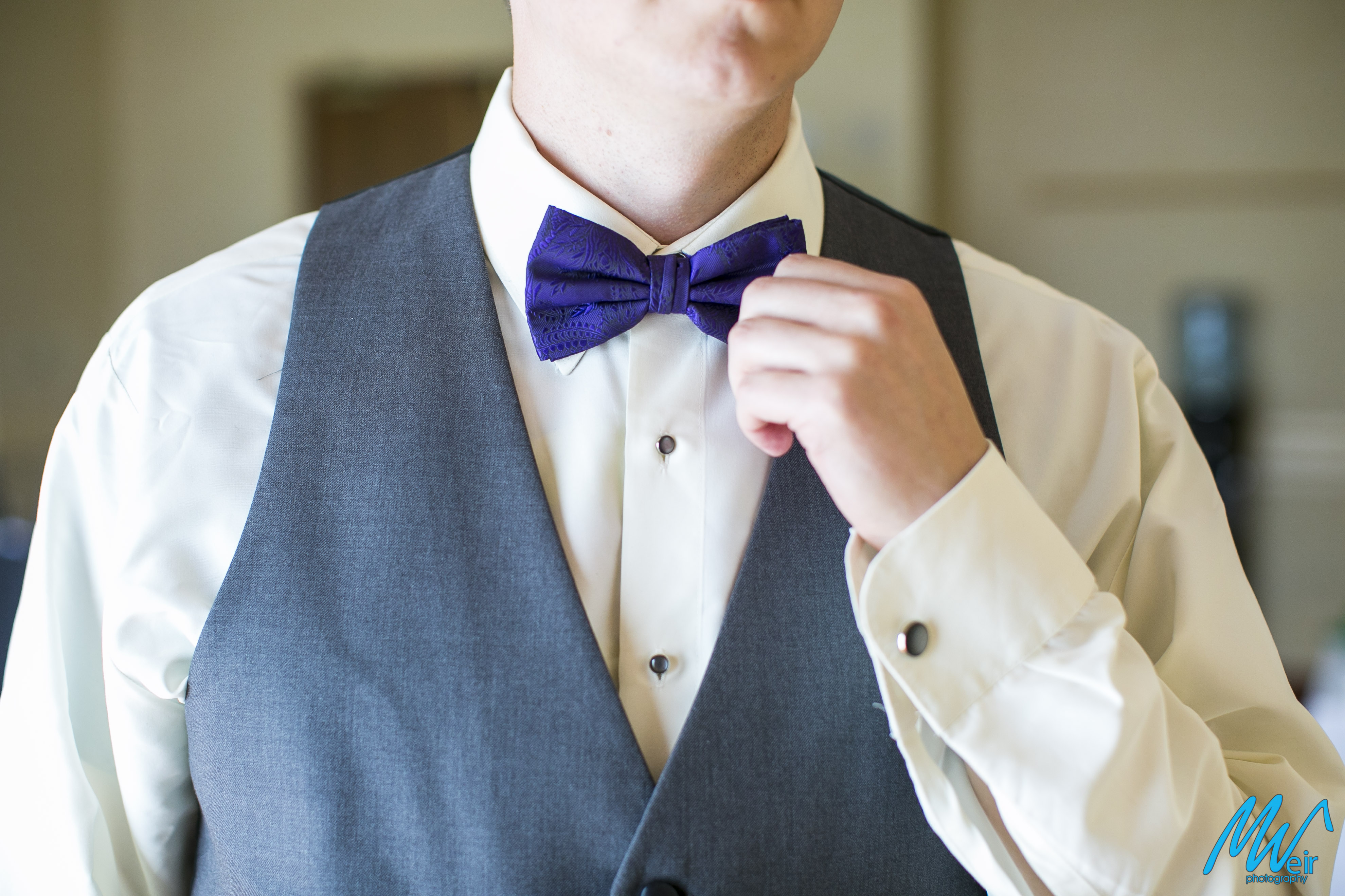 groom adjusting purple bow tie