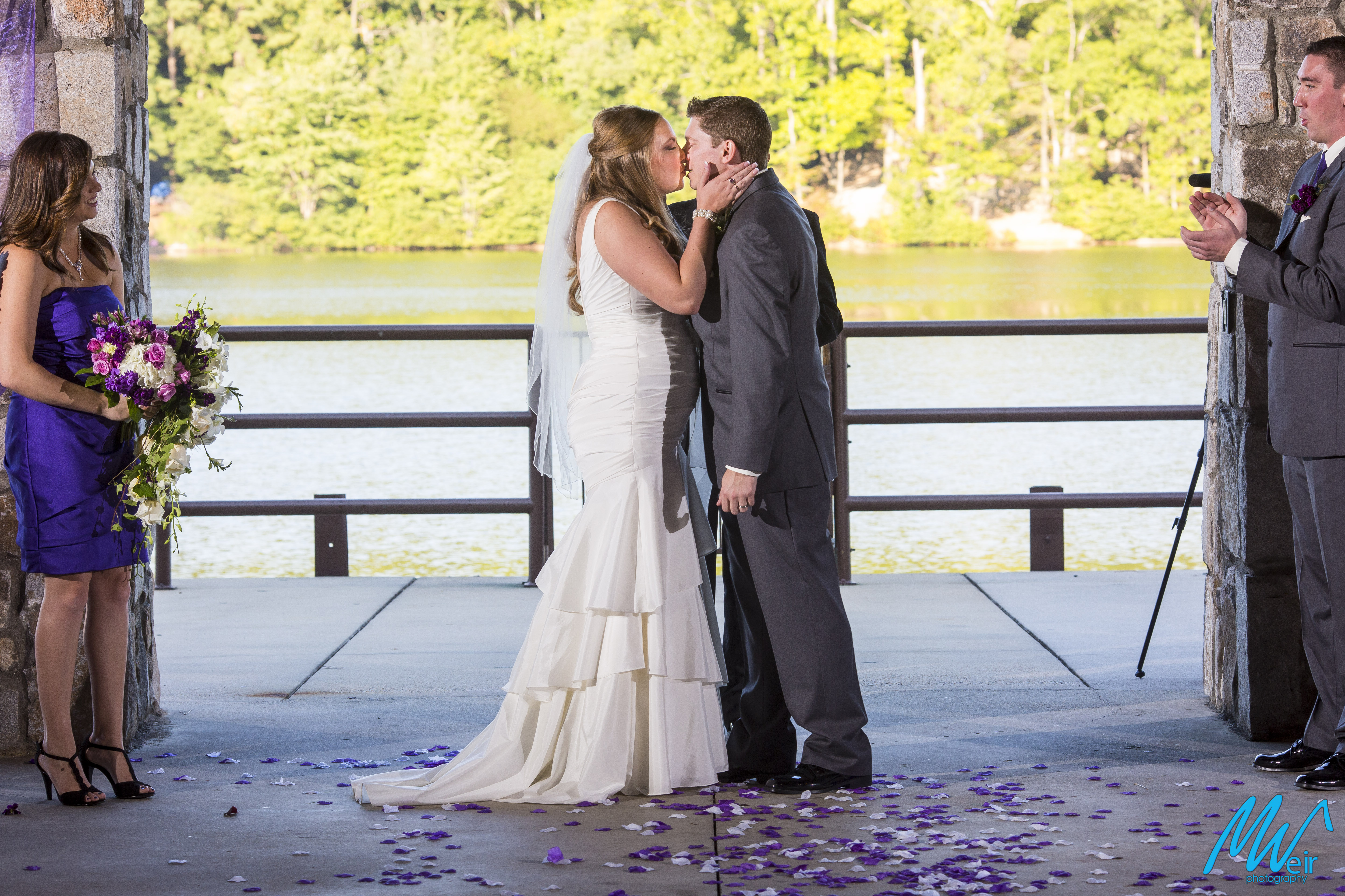 bride and groom kiss next to a lake after being pronounced man and wife