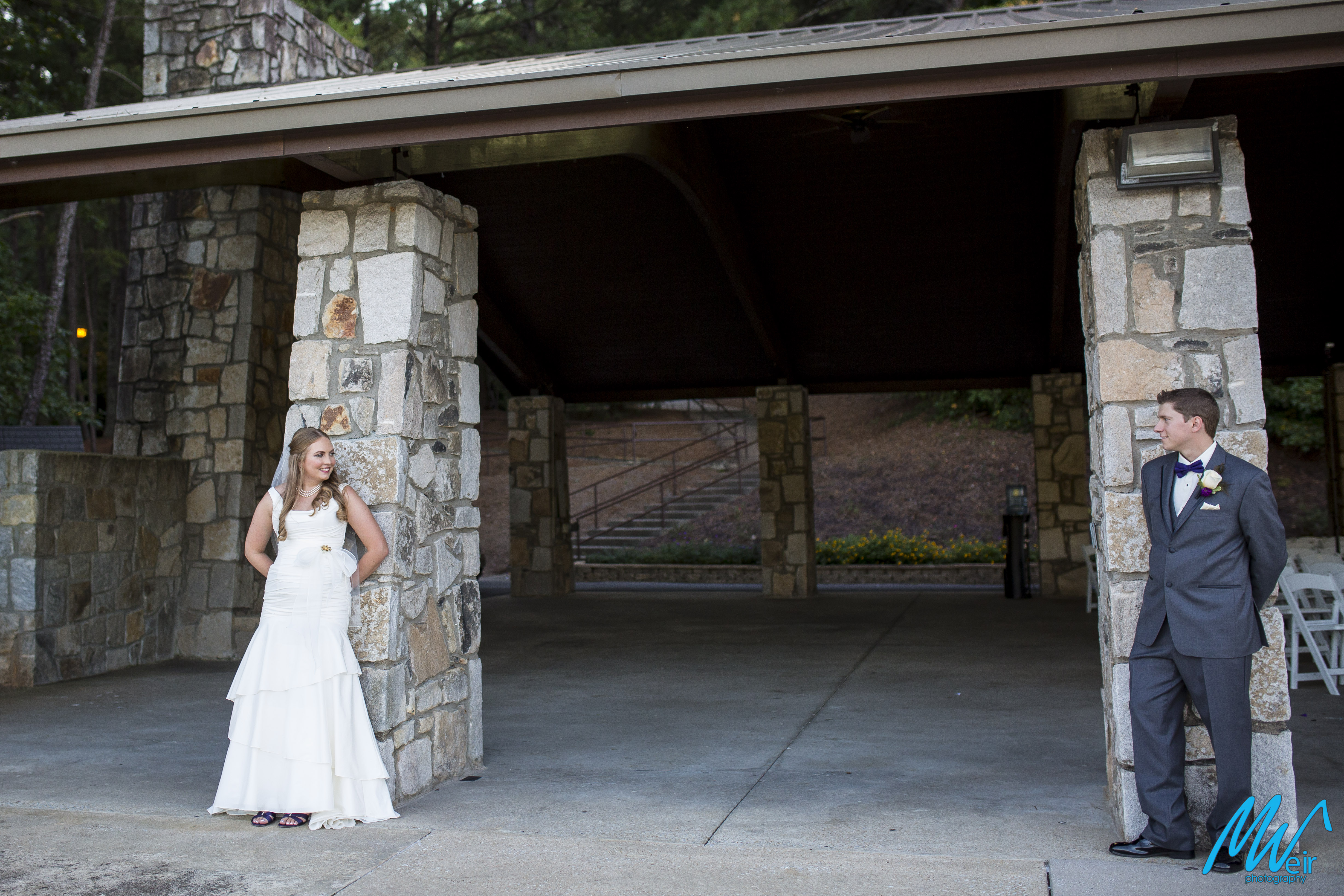bride and groom look at one another on stone pillars