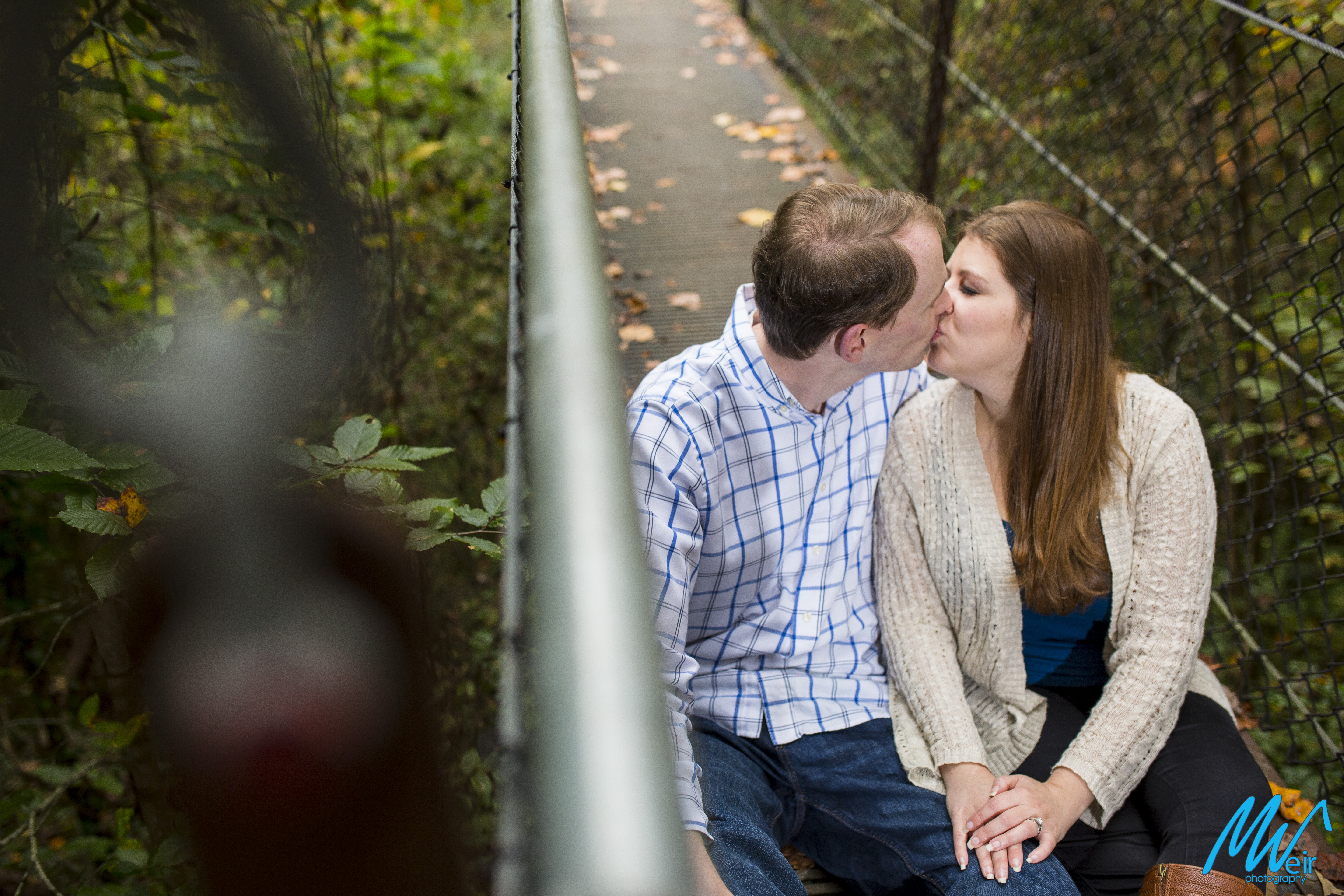 couple kiss sitting on a bridge
