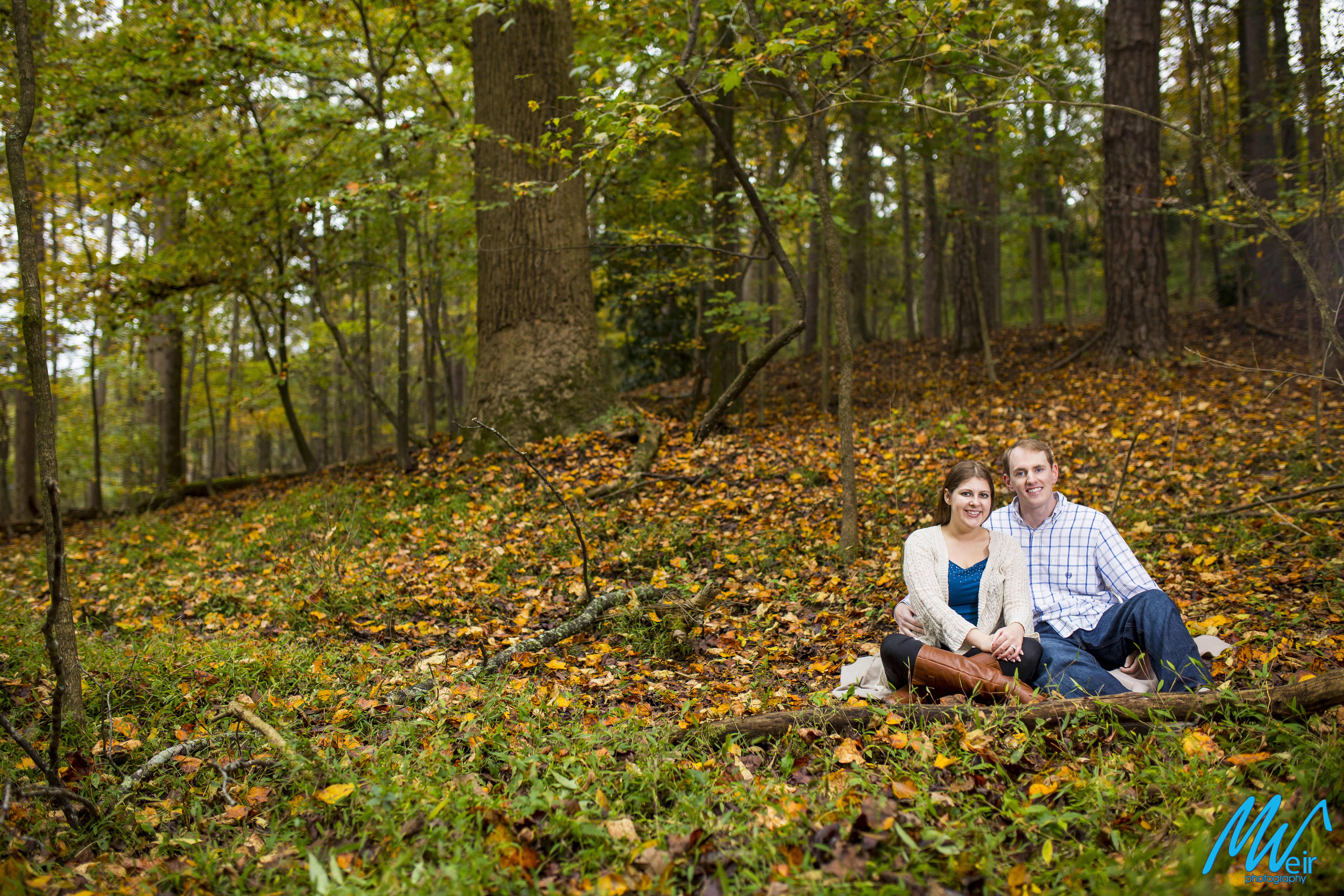 couple sit in the fall leaves during their engagement session