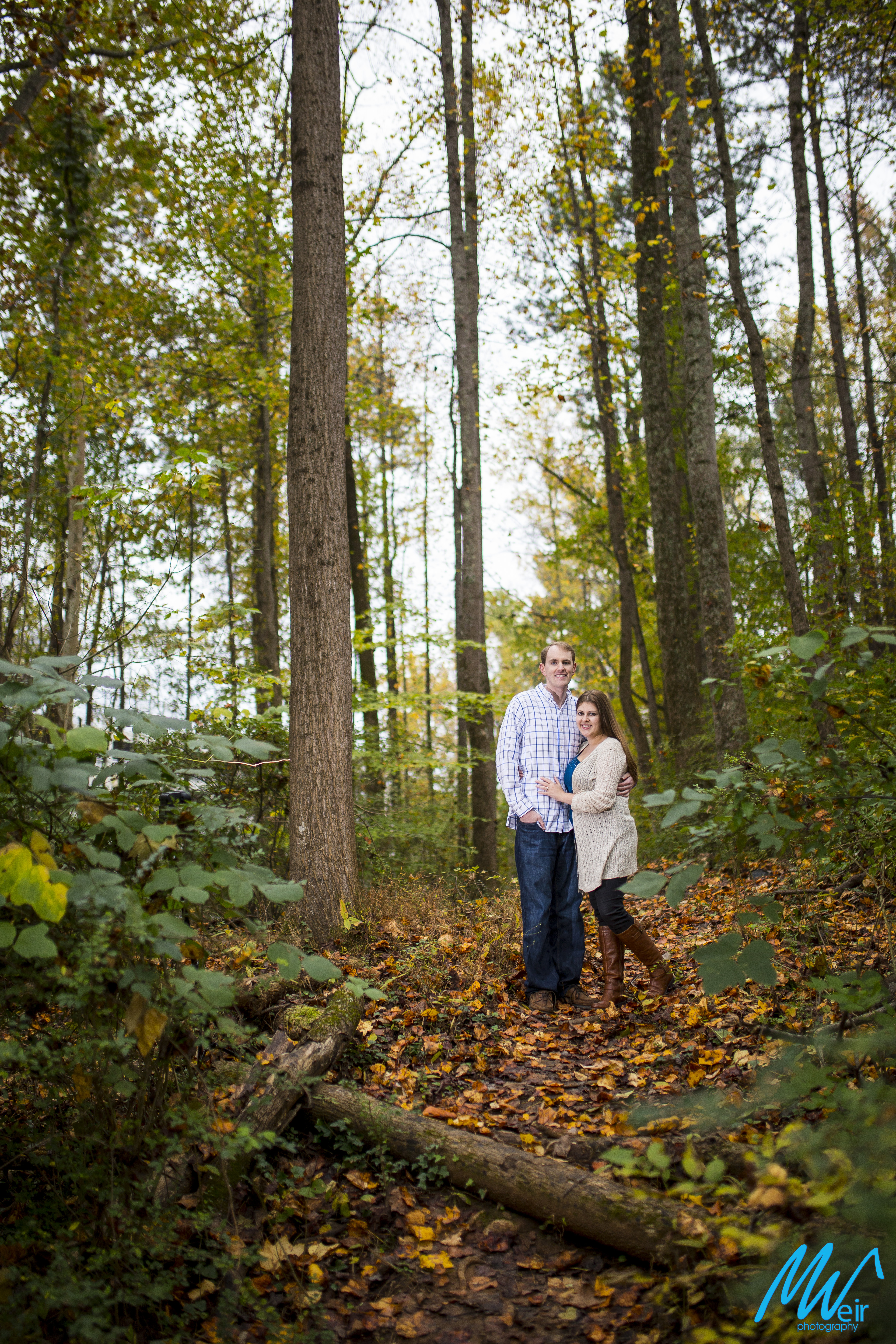 couple in fall woods smile at the camera