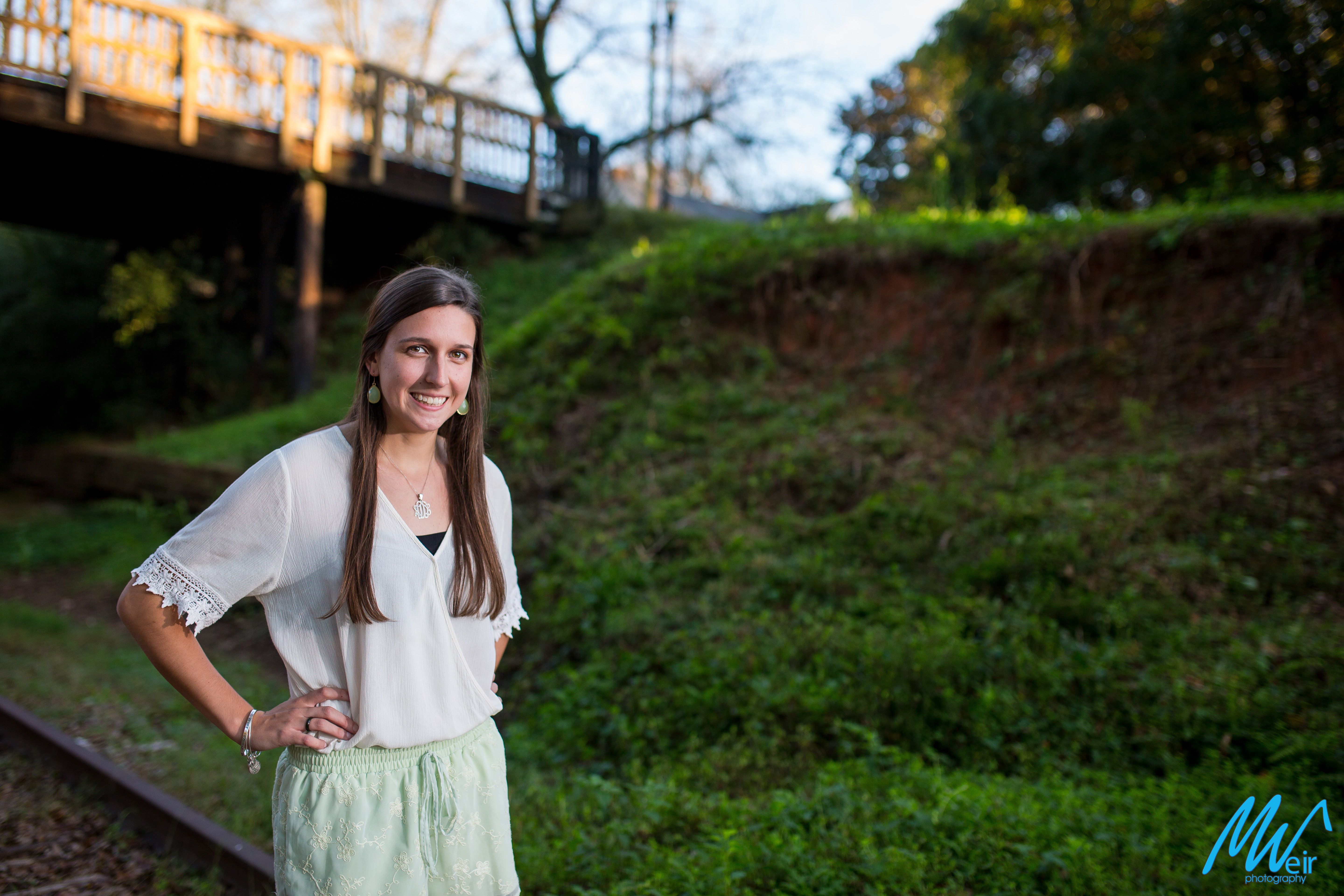 high school senior girl standing in front of green hill