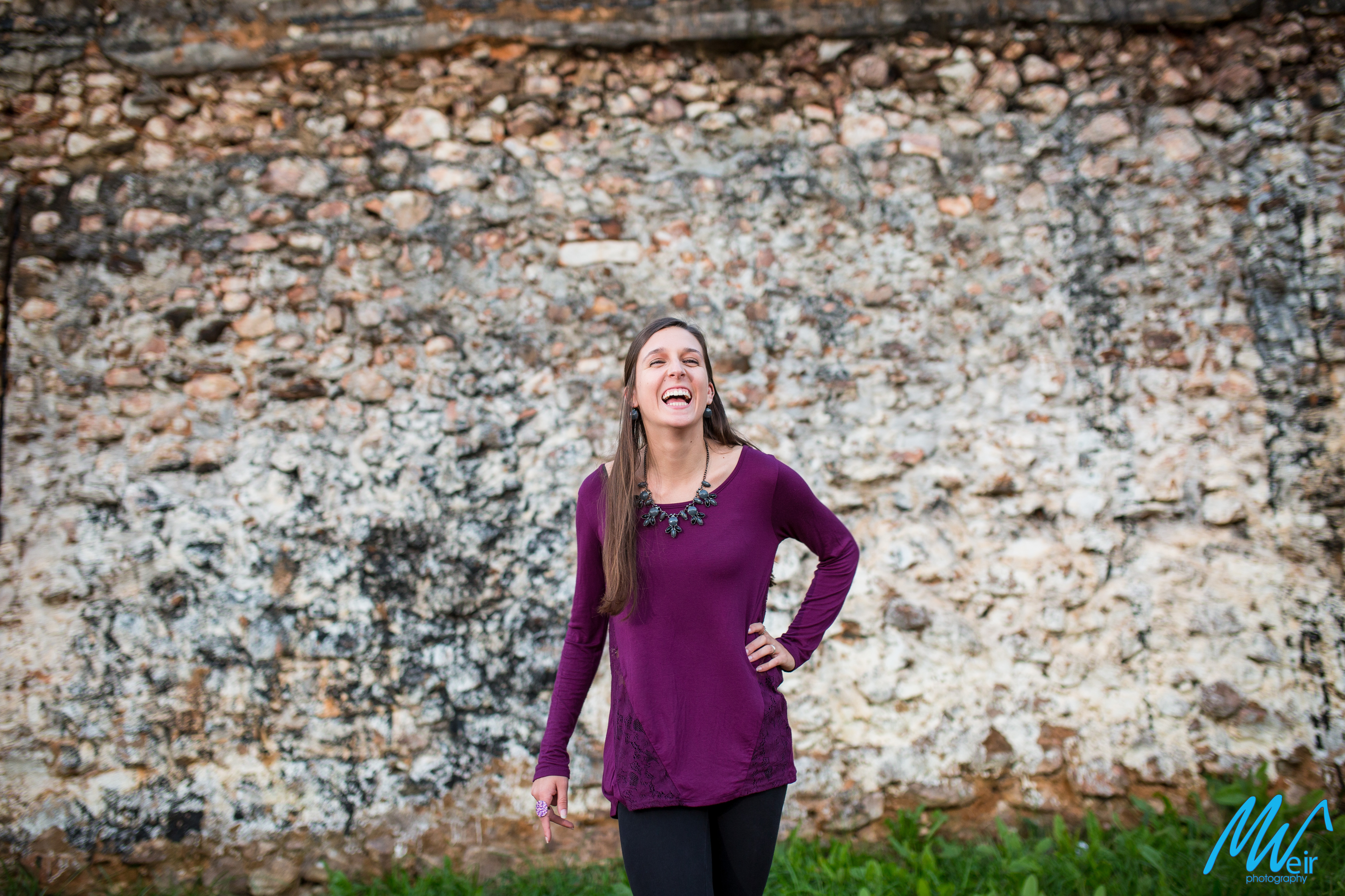 high school senior girl laughing in front of old stone wall