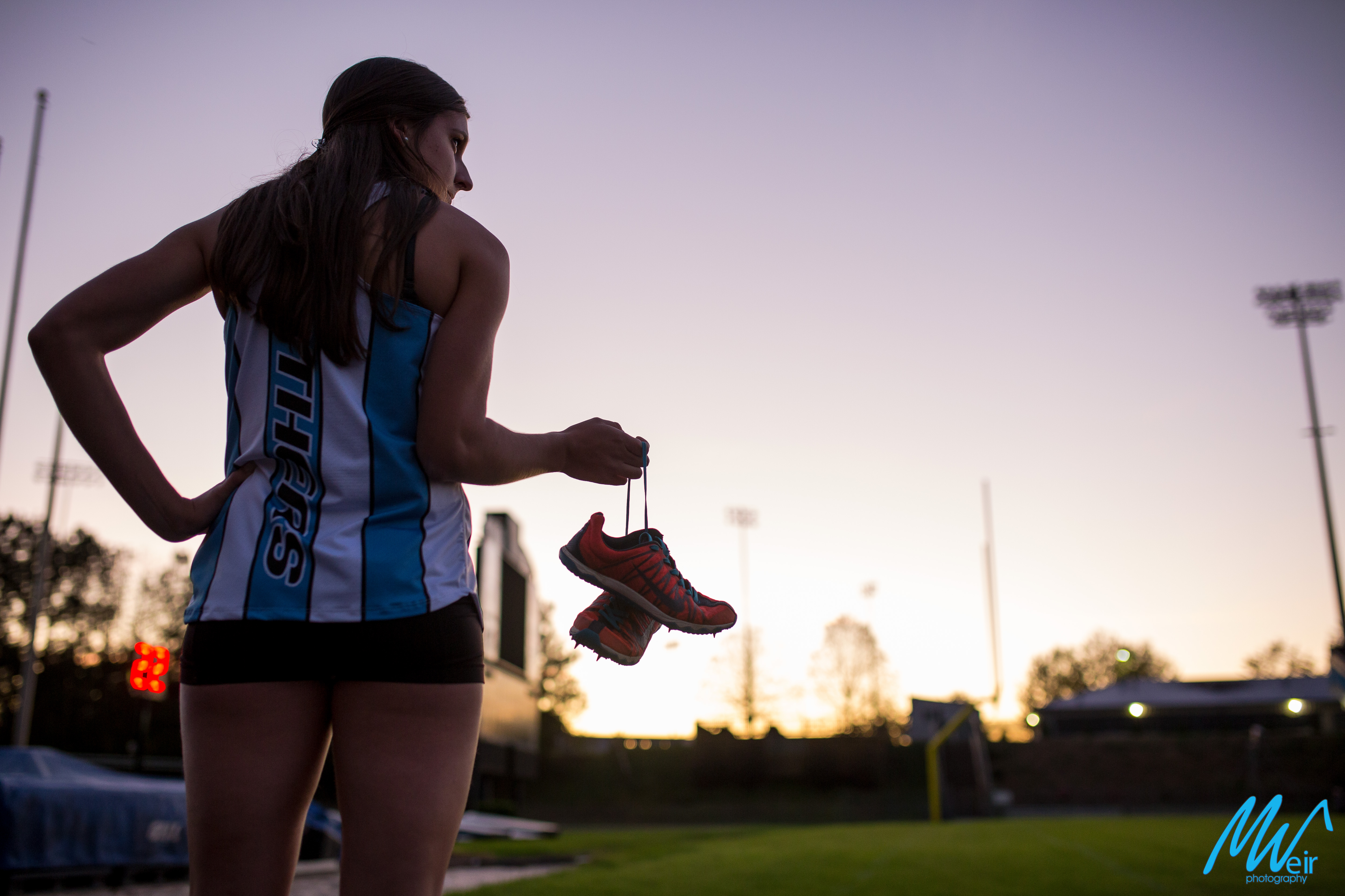 high school senior girl holding track shoes in the sunset