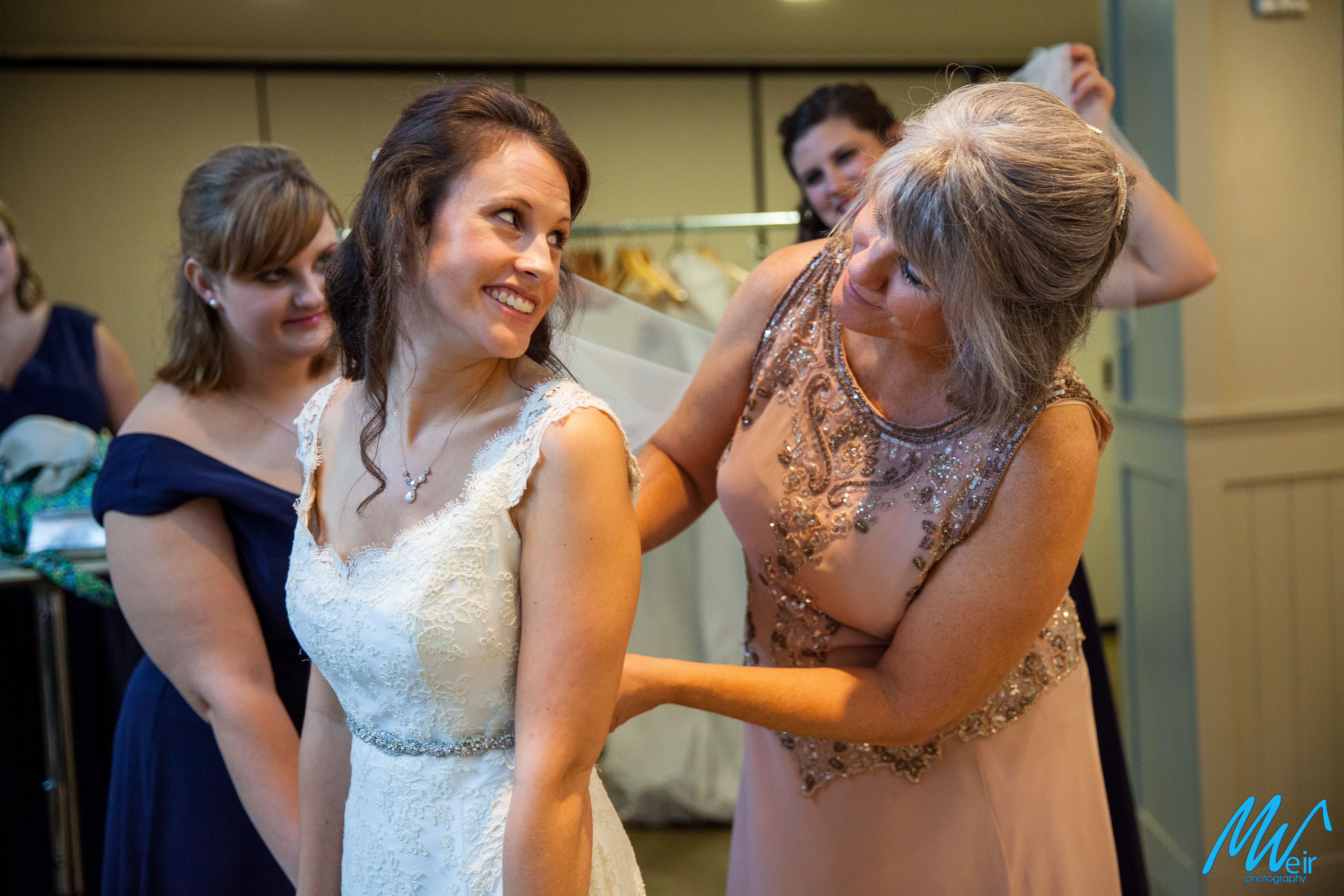 bride smiling at her mom while she helps put on her dress