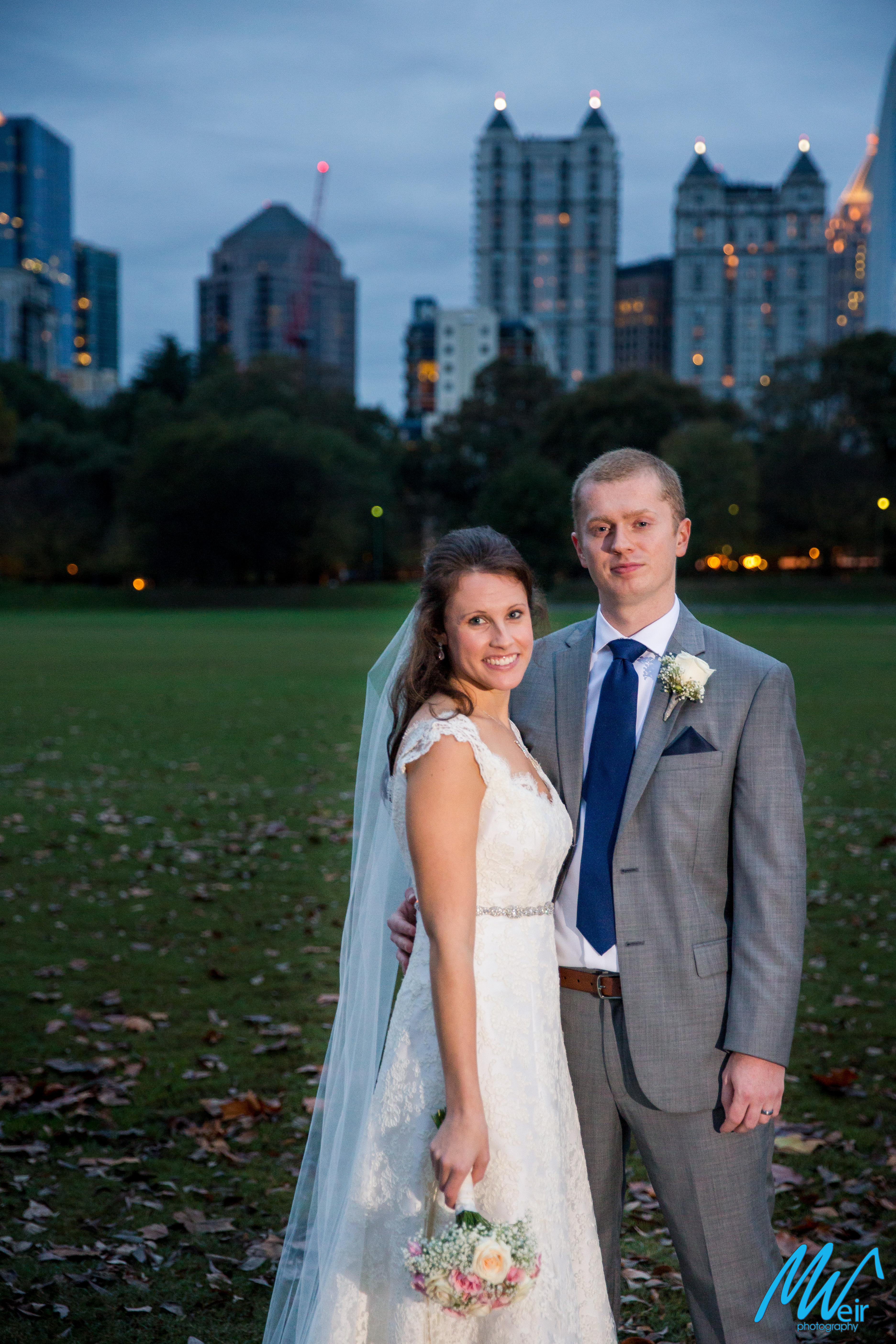 bride and groom in piedmont park with atlanta skyline behind them
