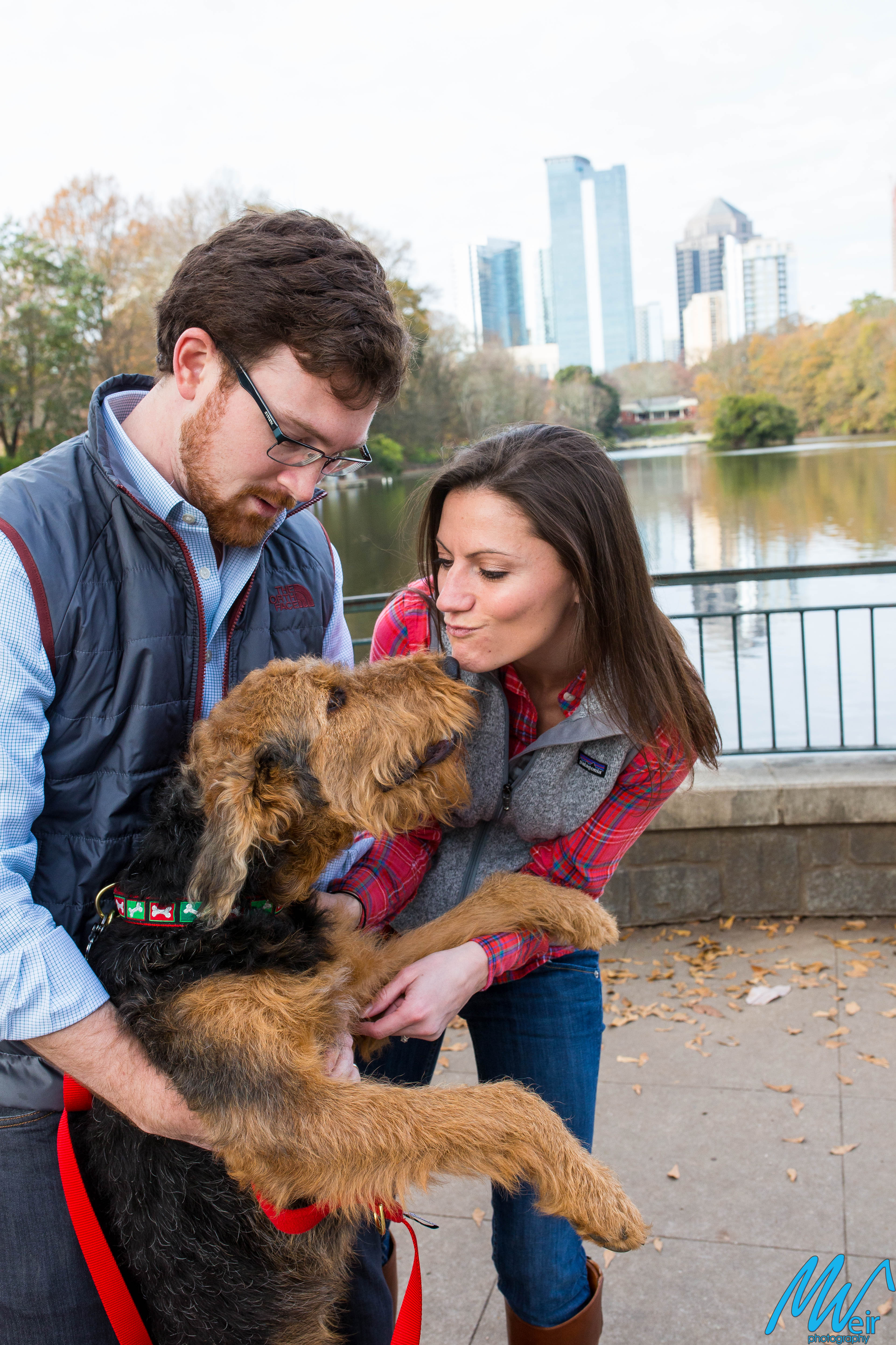husband and wife and their puppy in front of the atlanta skyline in piedmont park
