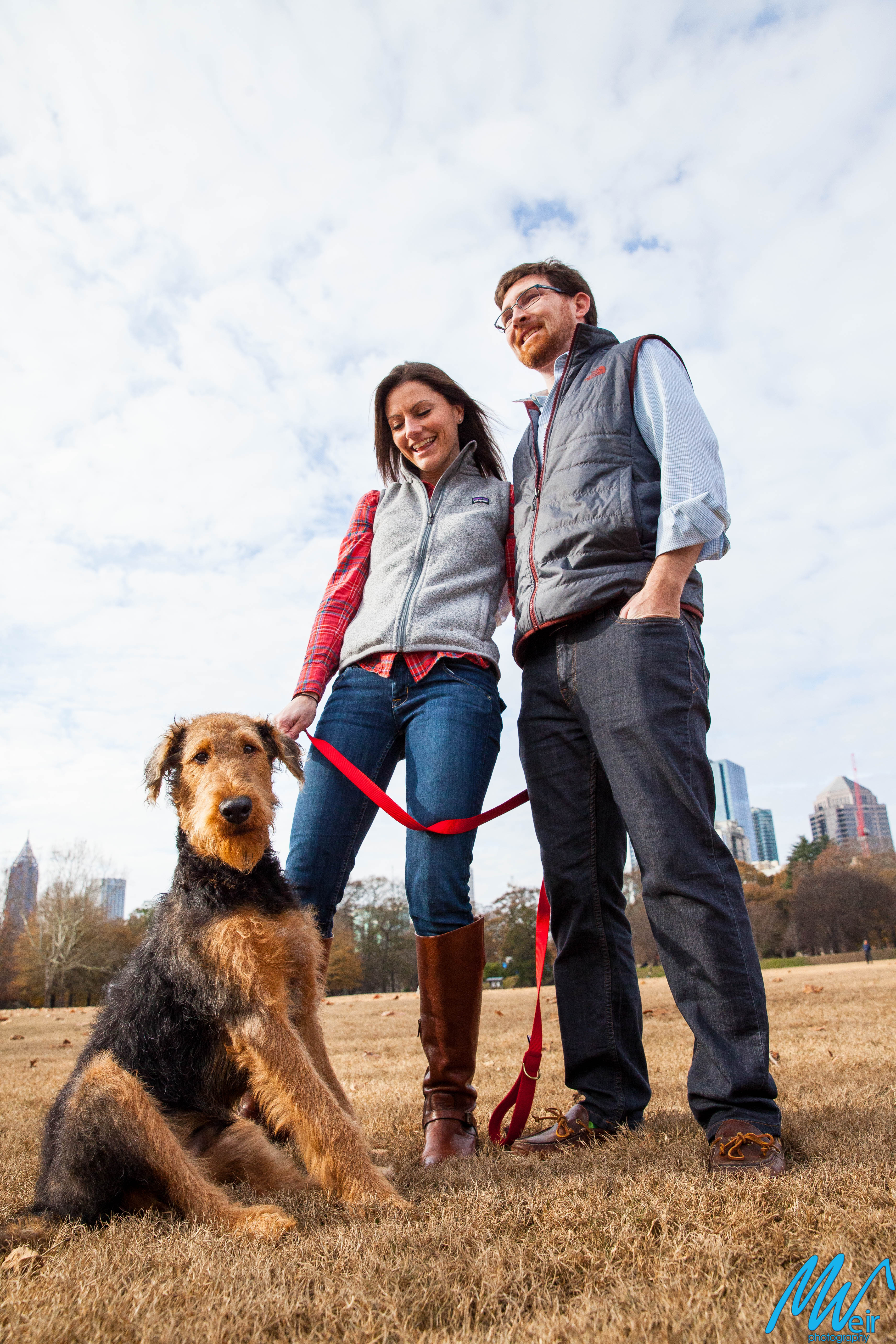 husband and wife and their puppy in front of the atlanta skyline in piedmont park