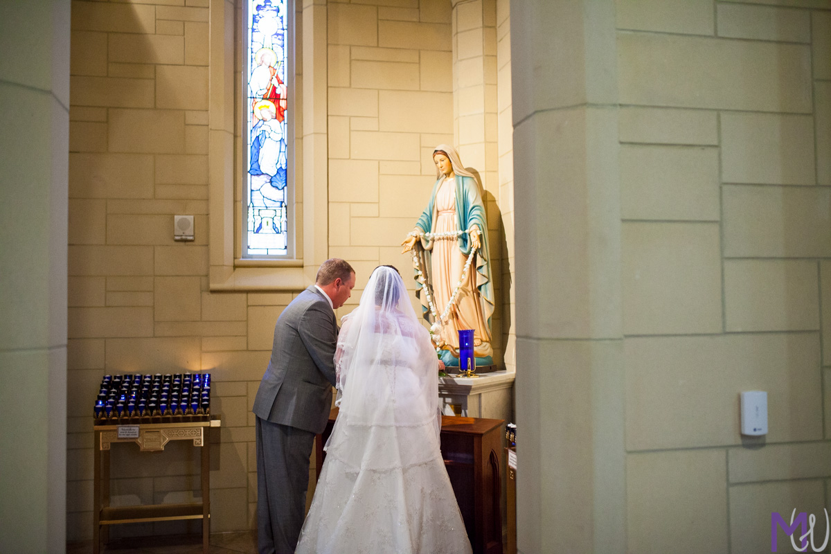 bride and groom give roses to mother mary statue