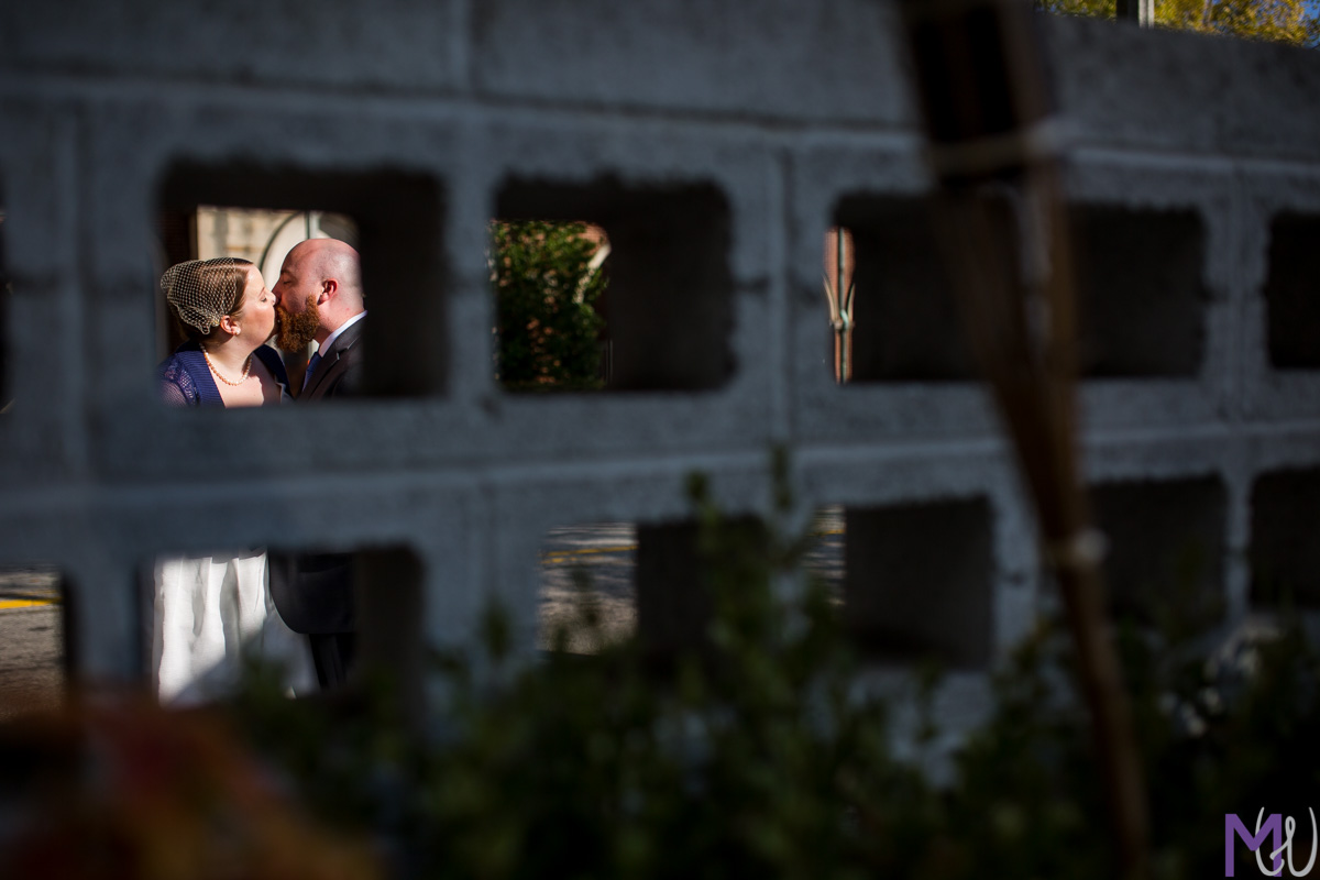 bride and groom kissing through a concrete wall