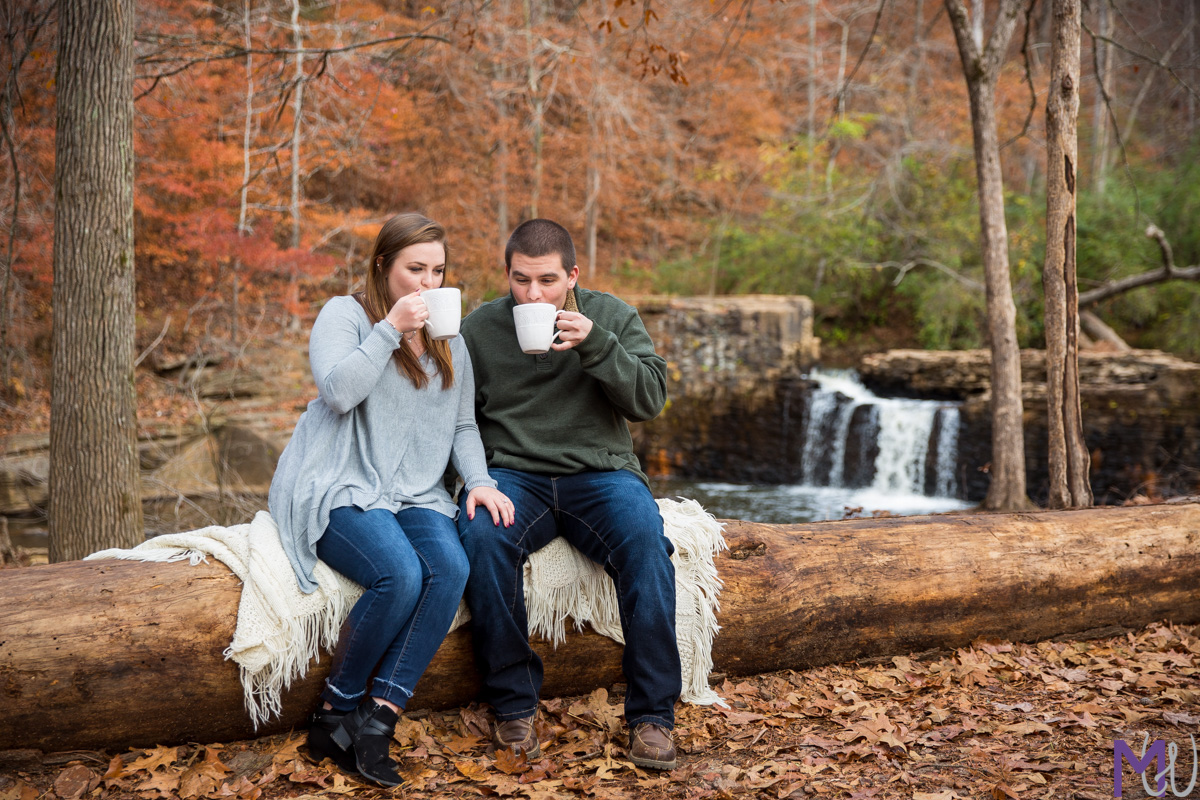 couple sitting on a log in front of a waterfall with hot chocolate
