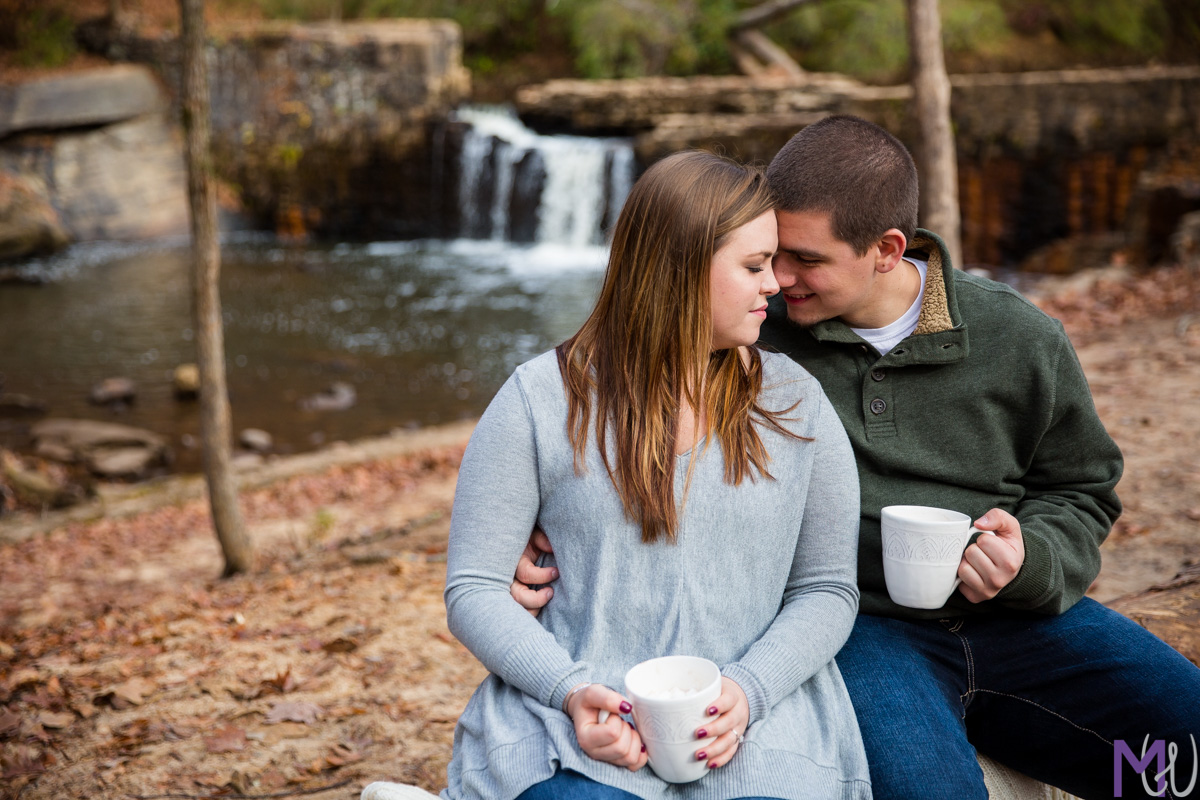 couple sitting on a log in front of a waterfall with hot chocolate