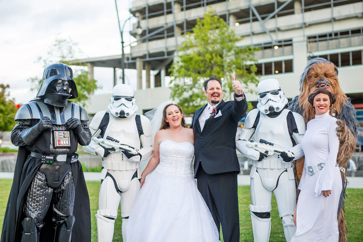 couple waves to friends standing next to darth vader, chewbacca, and storm troopers