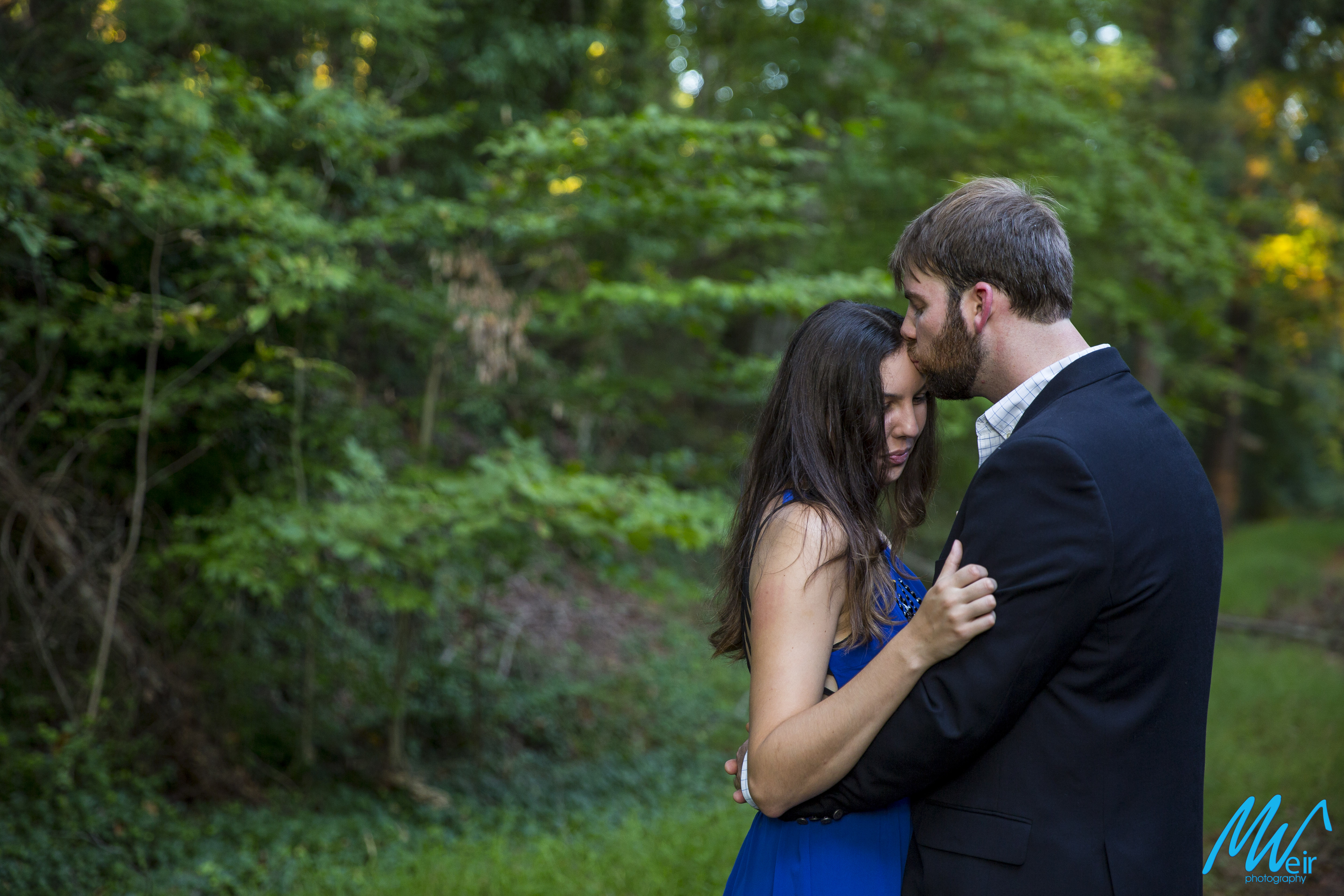 groom kisses the brides forehead while she looks down in the woods