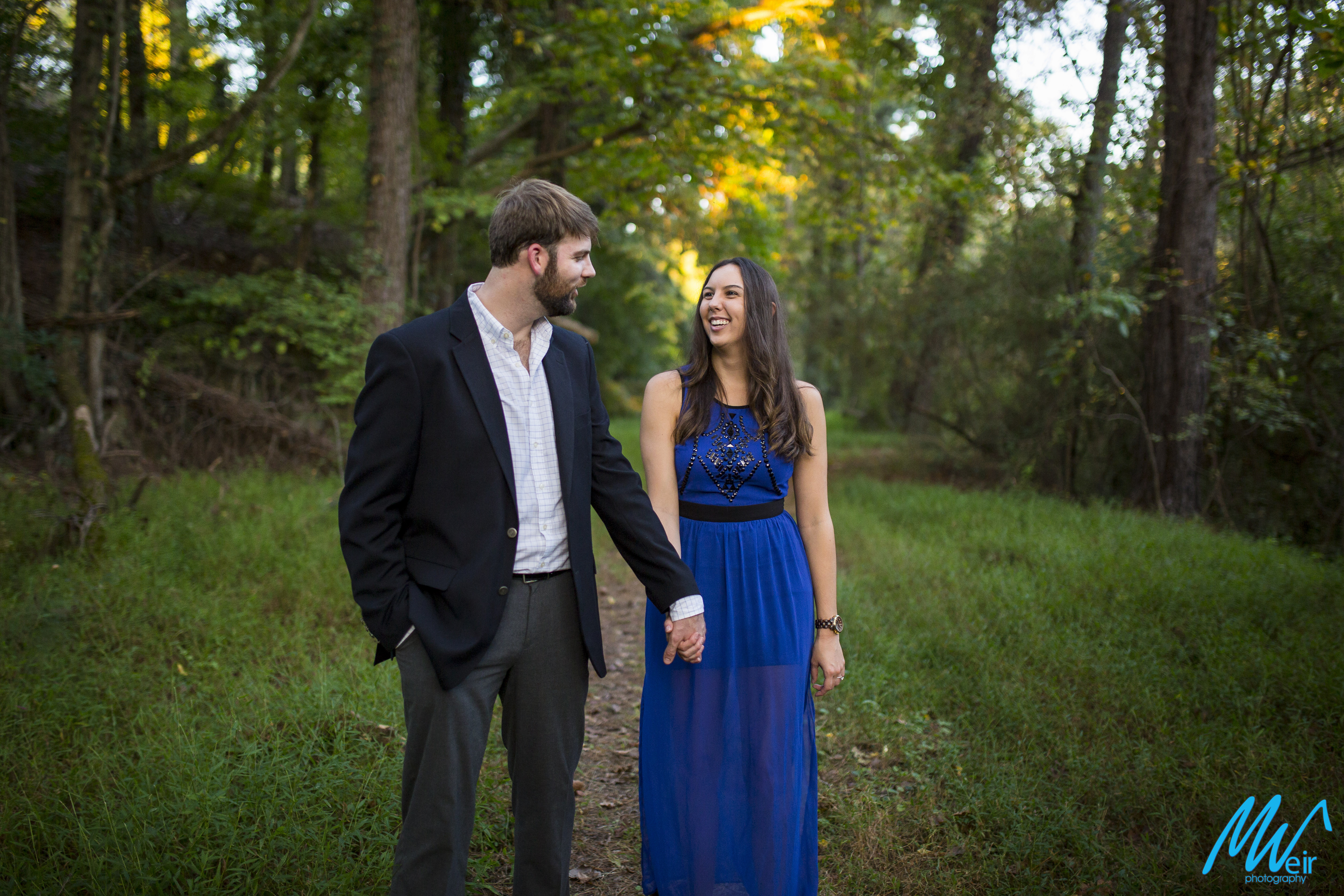 engaged couple walking through the woods together in blue dress