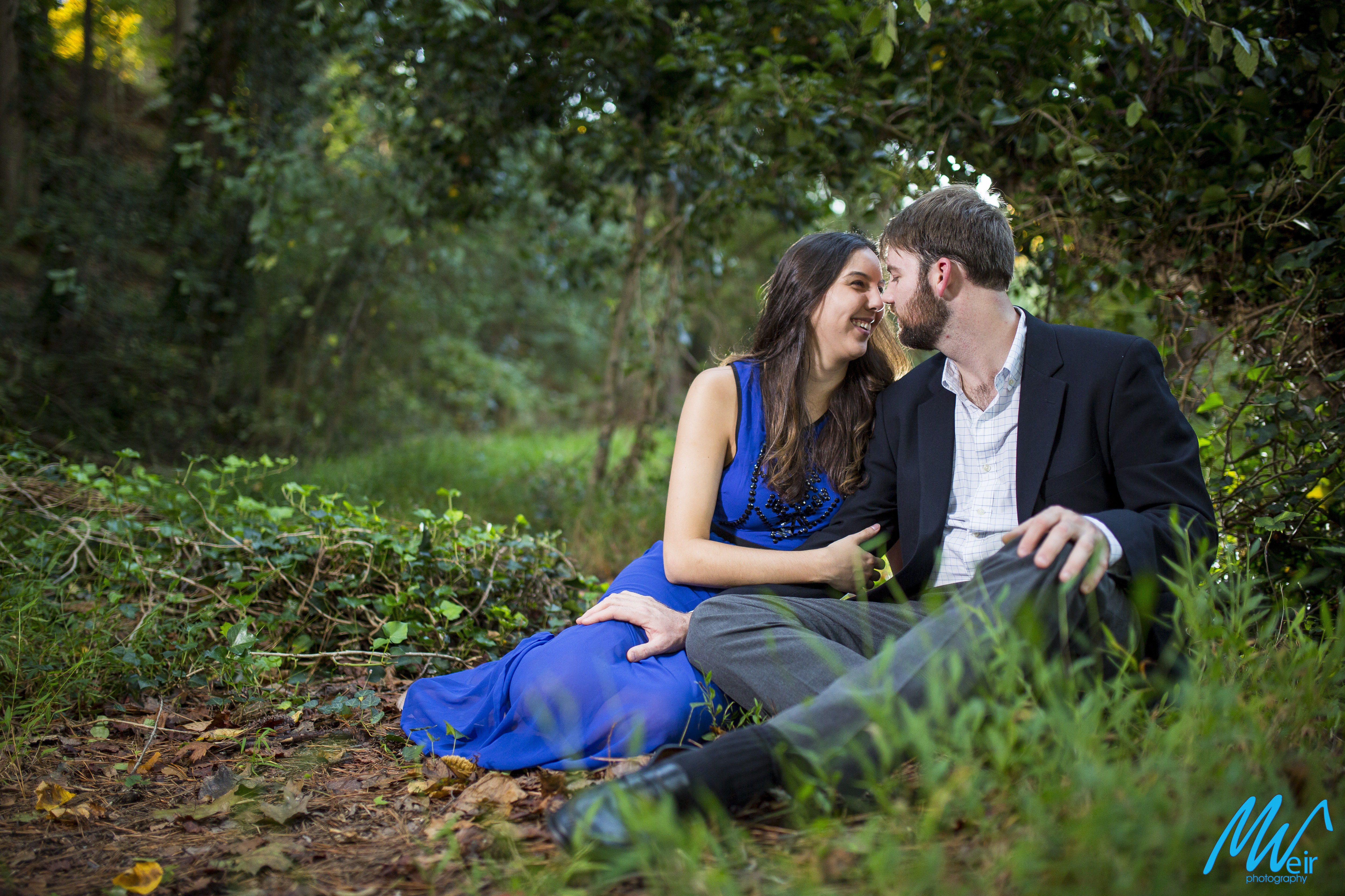 engaged couple about to kiss in the grass in the woods