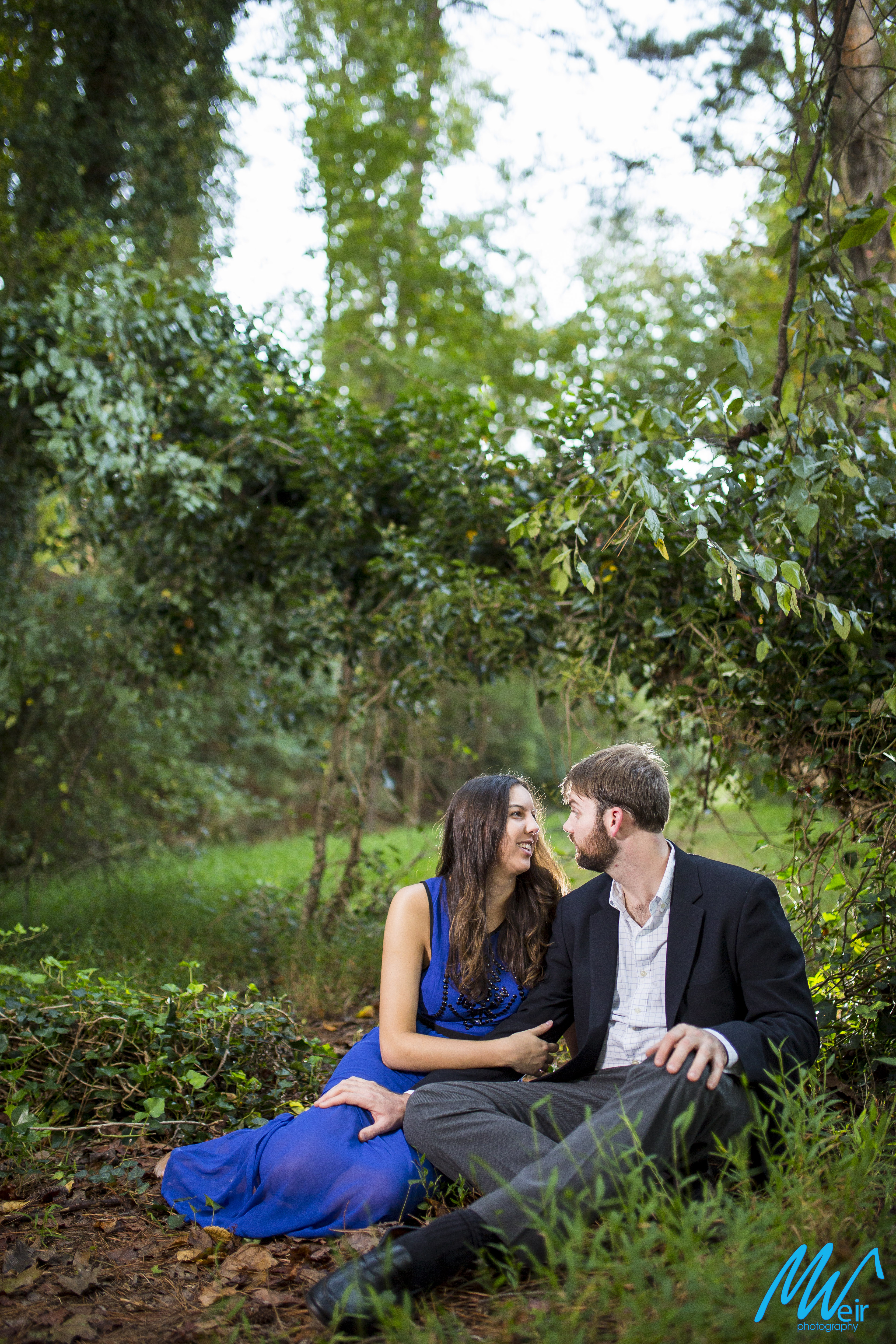 engaged couple sitting in the grass under a low hanging tree