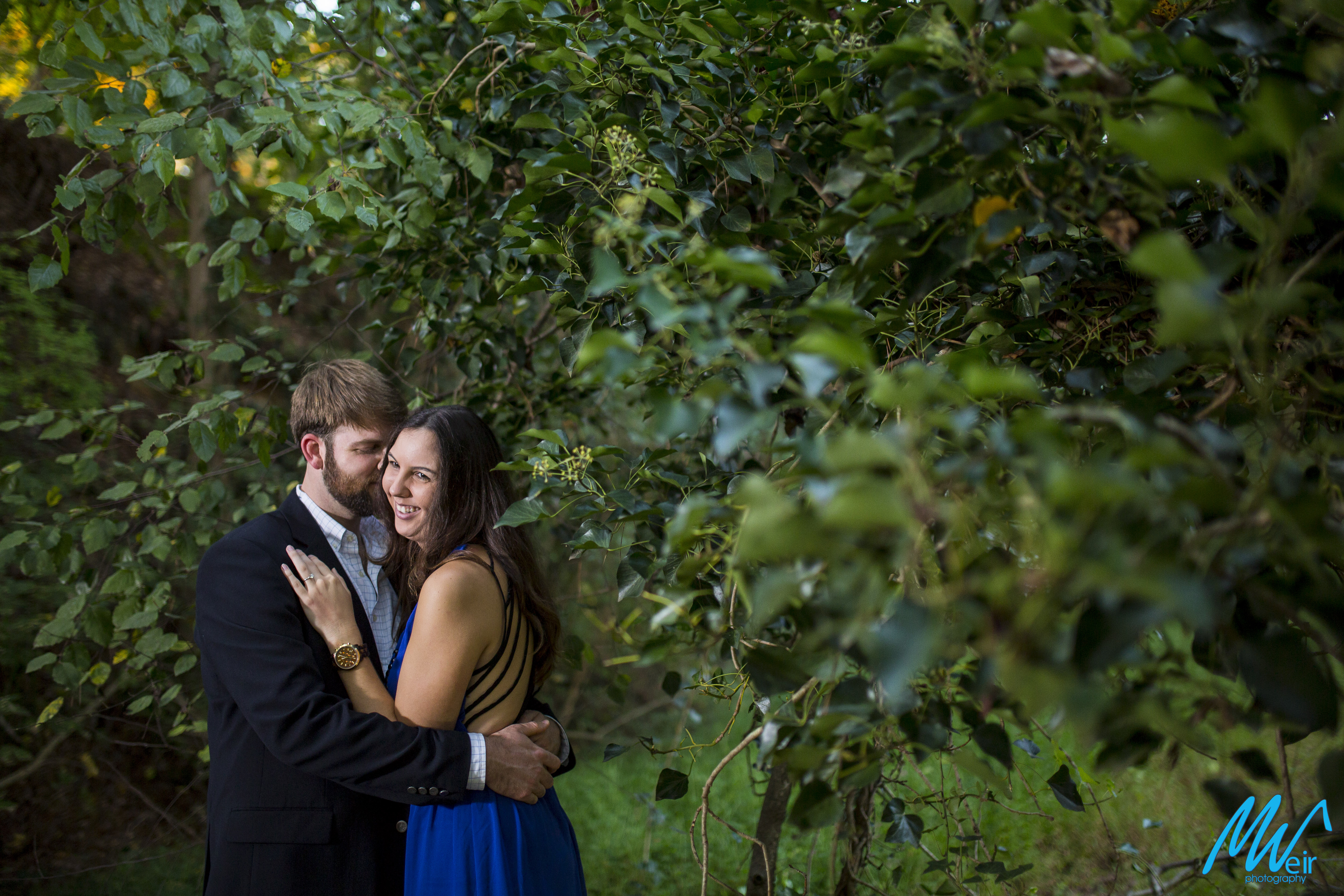 groom whispers in brides ear sweet nothings while under a low tree