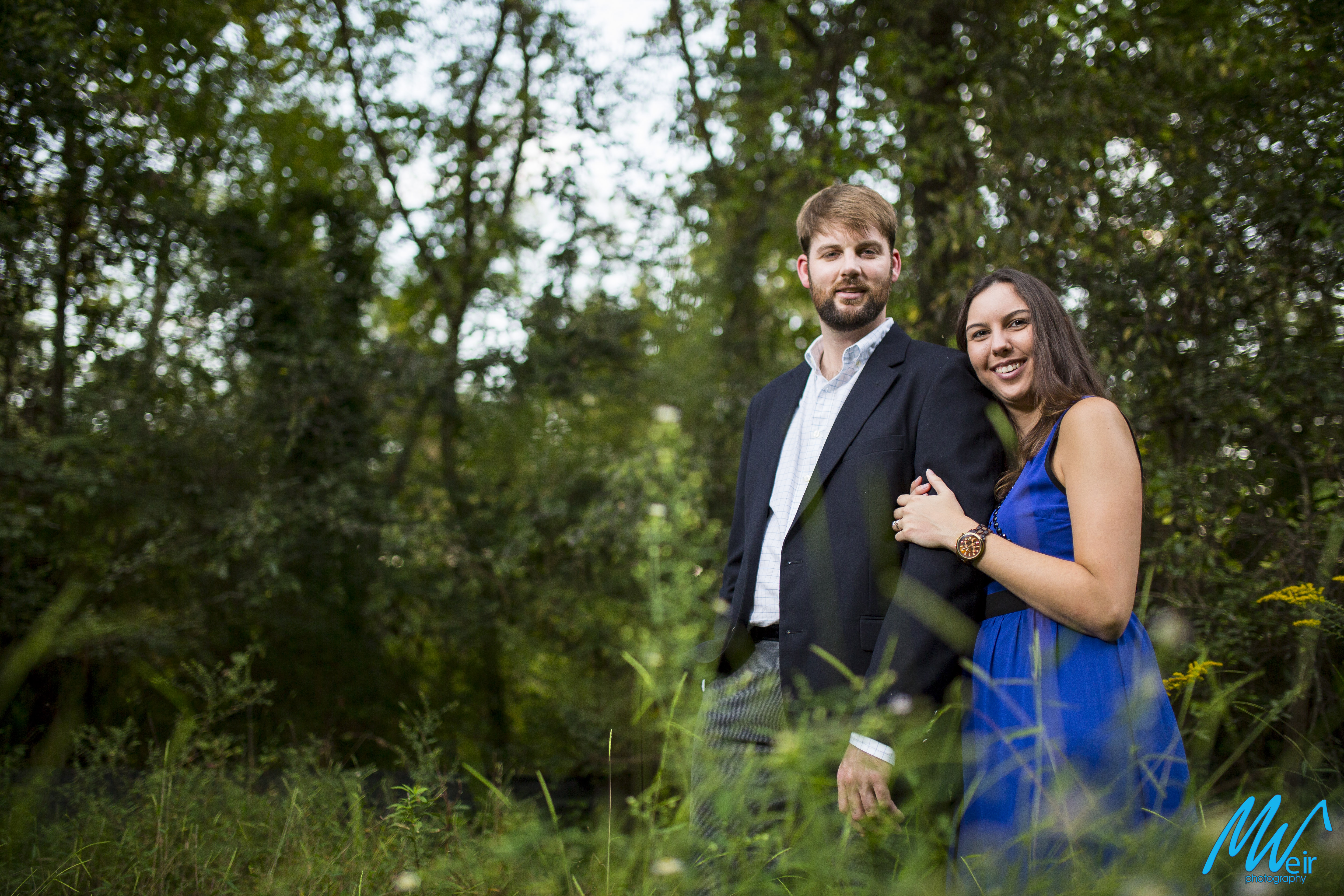 engaged couple standing in the tall grass in the woods