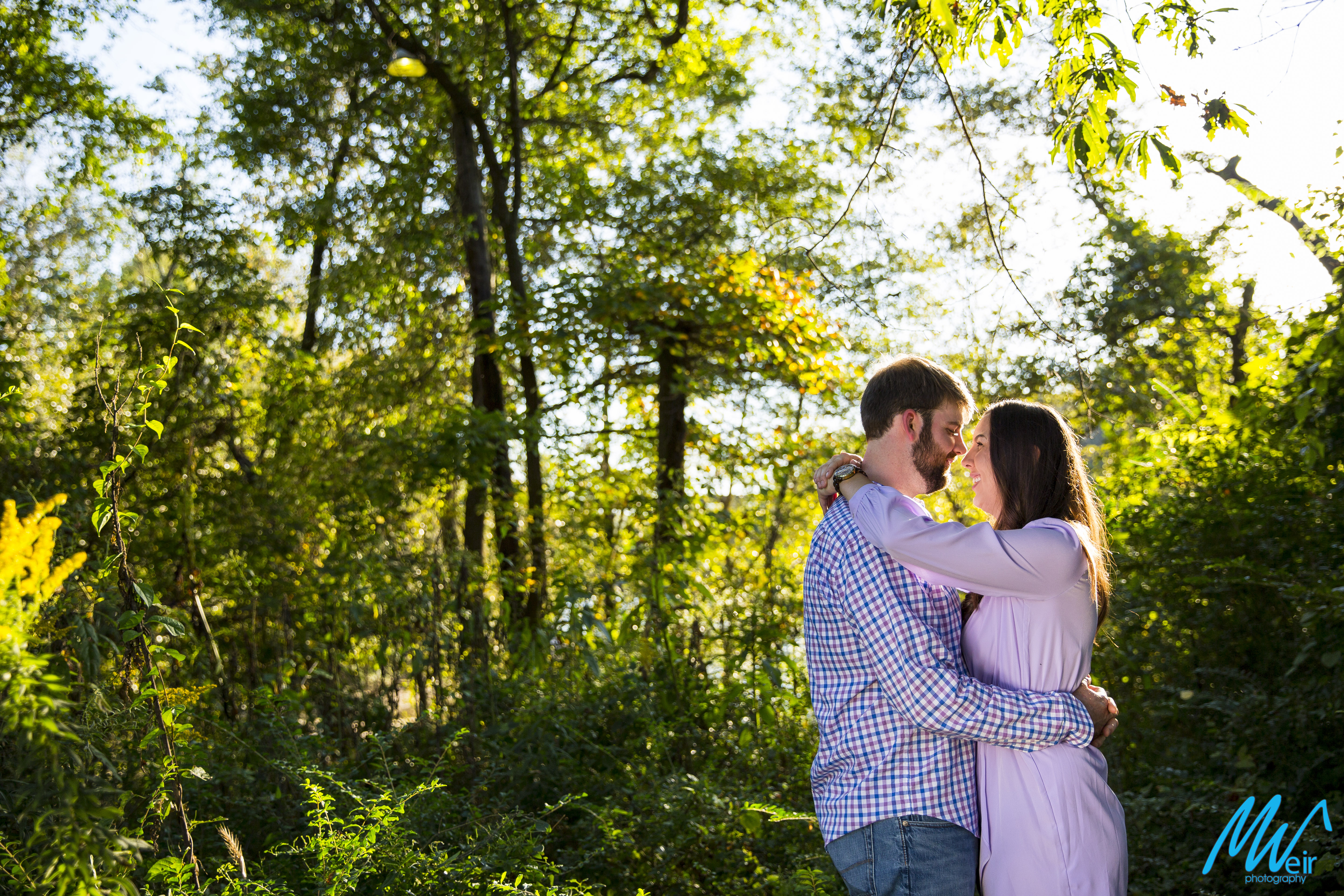 bride and groom hug while standing in a sun kissed forest 