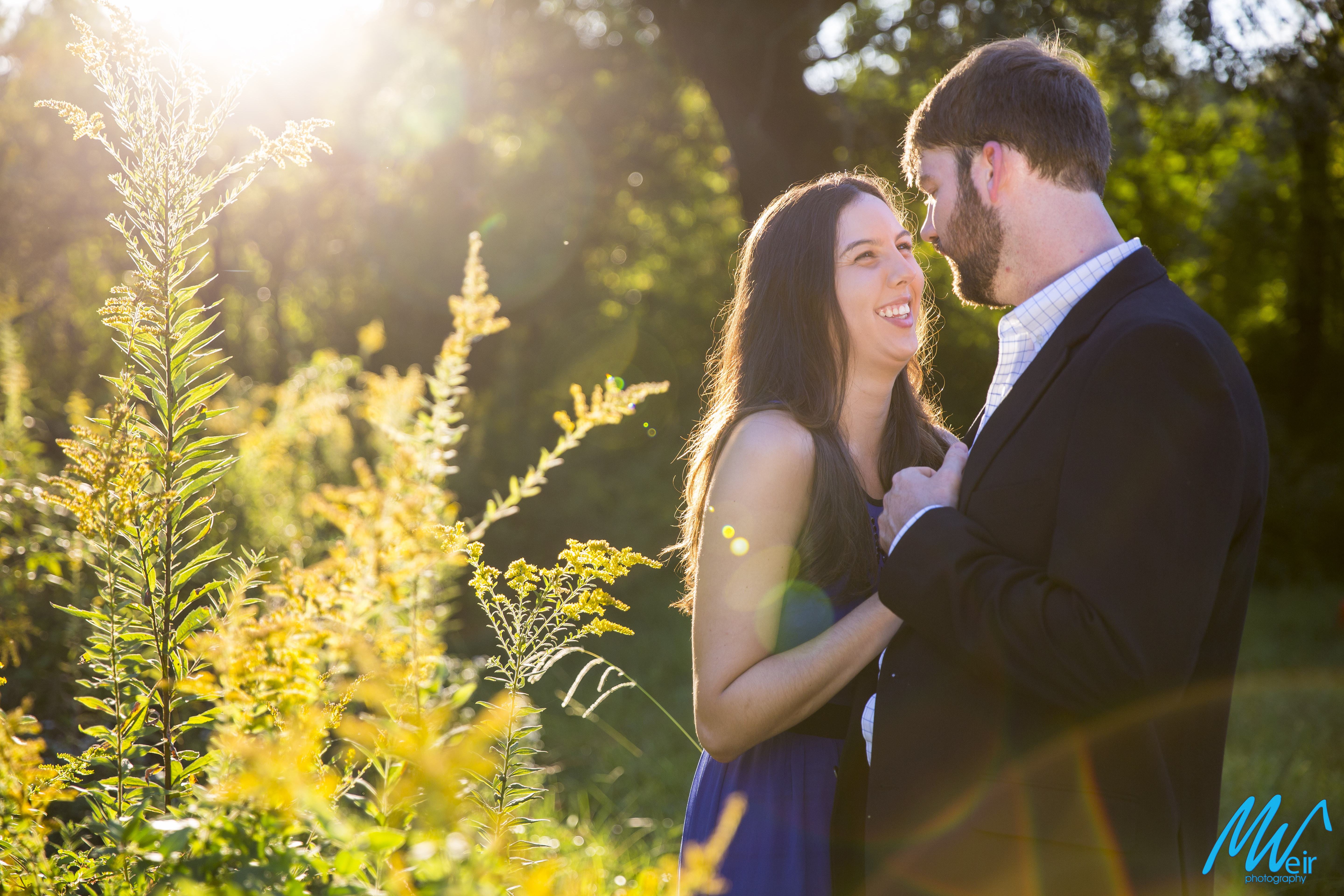 bride laughing at groom while standing in a field with light pouring in